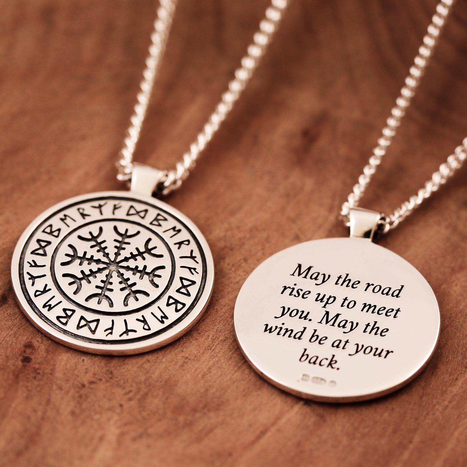 Two silver necklaces with engraved viking rune designs on a wooden surface
