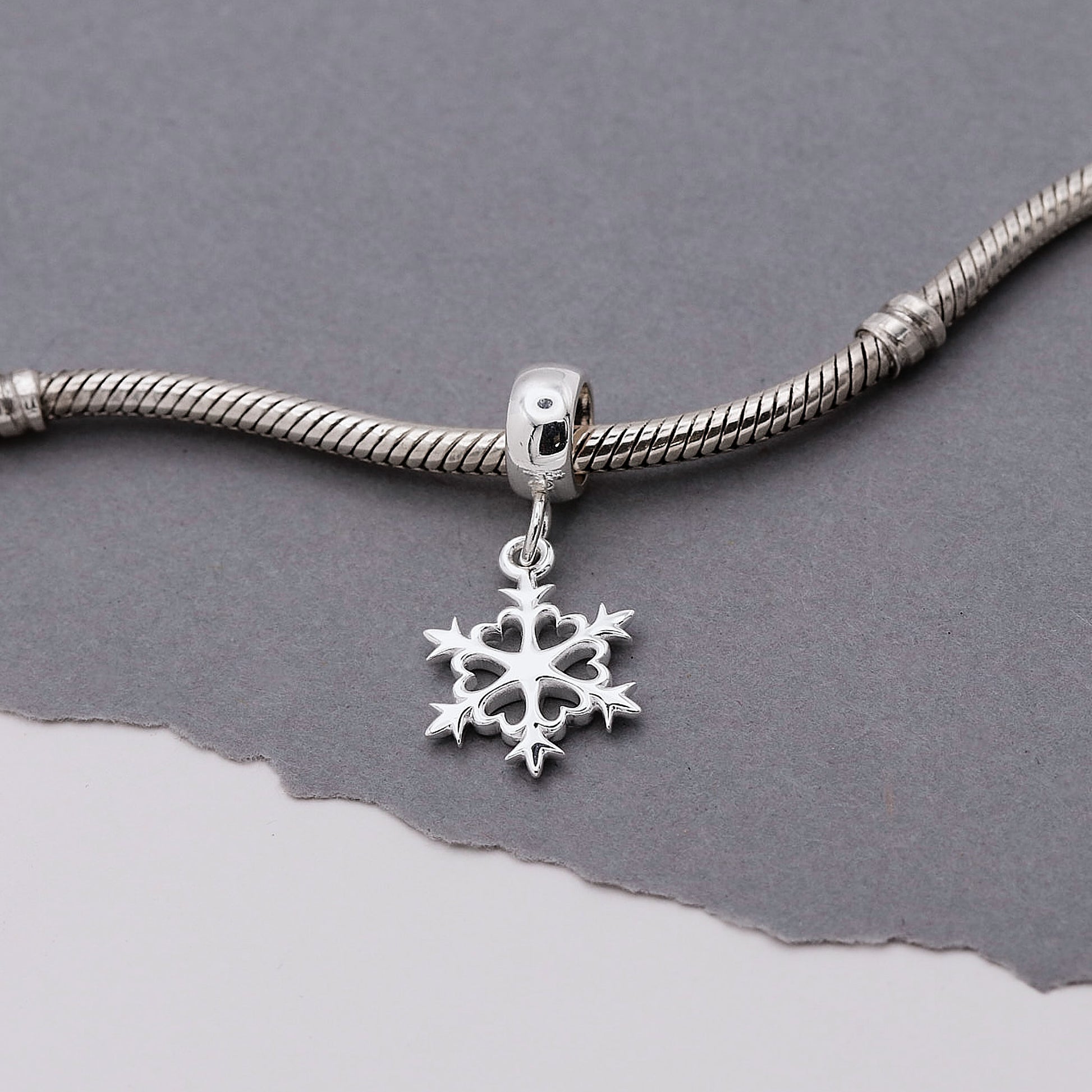 Silver snowflake charm on a silver bracelet against a gray background