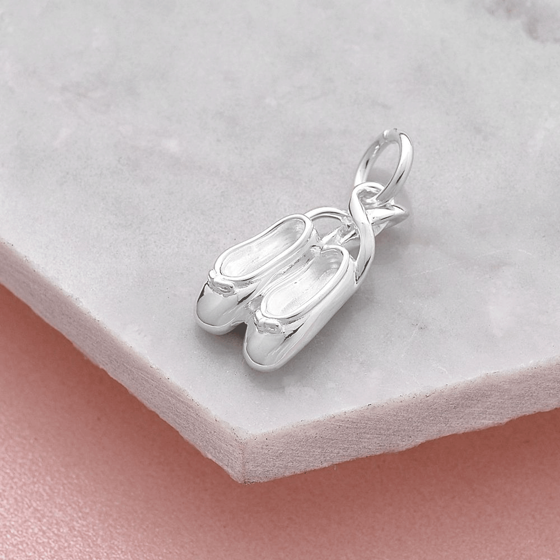 Silver ballet slipper charm on a light gray surface