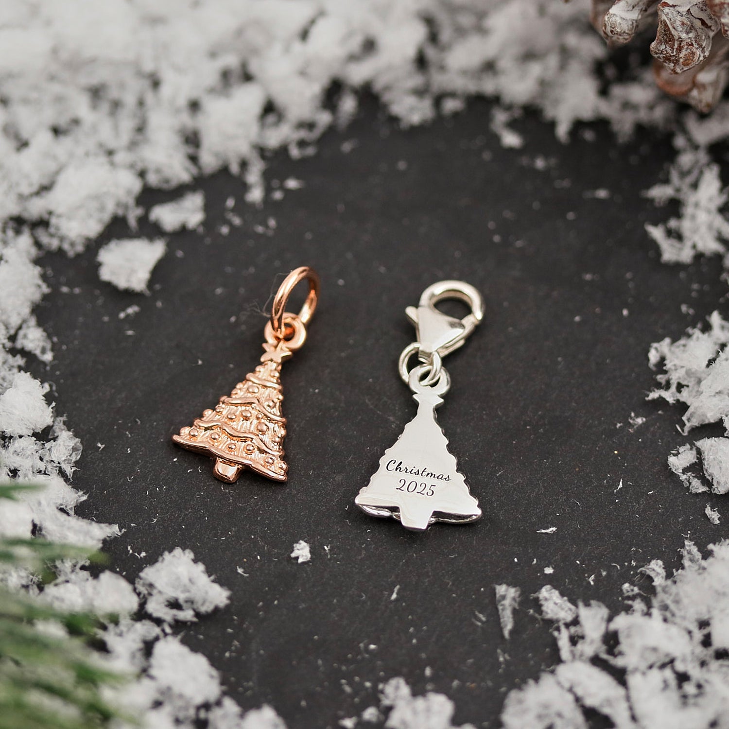 Two Christmas-themed charms on a dark surface with snow and greenery.