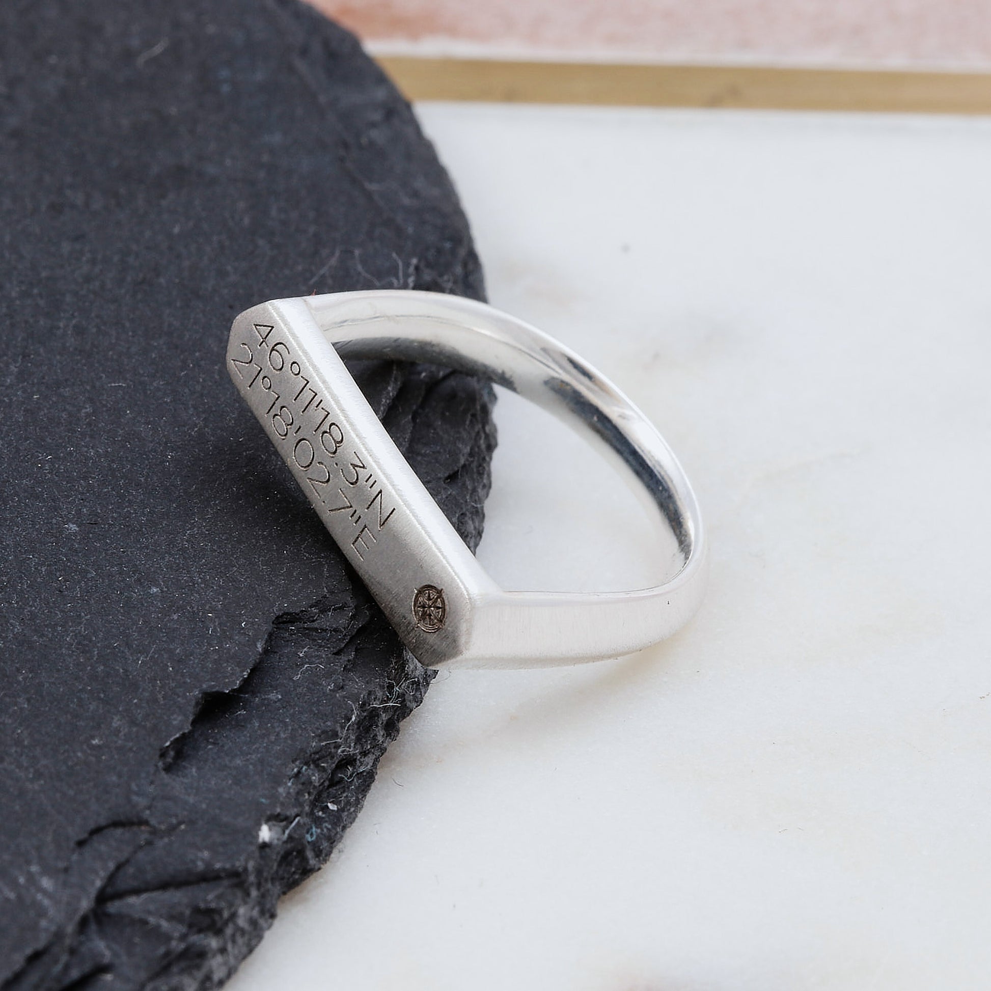 Silver matte finish bar signet ring with engraved coordinates on a dark stone surface