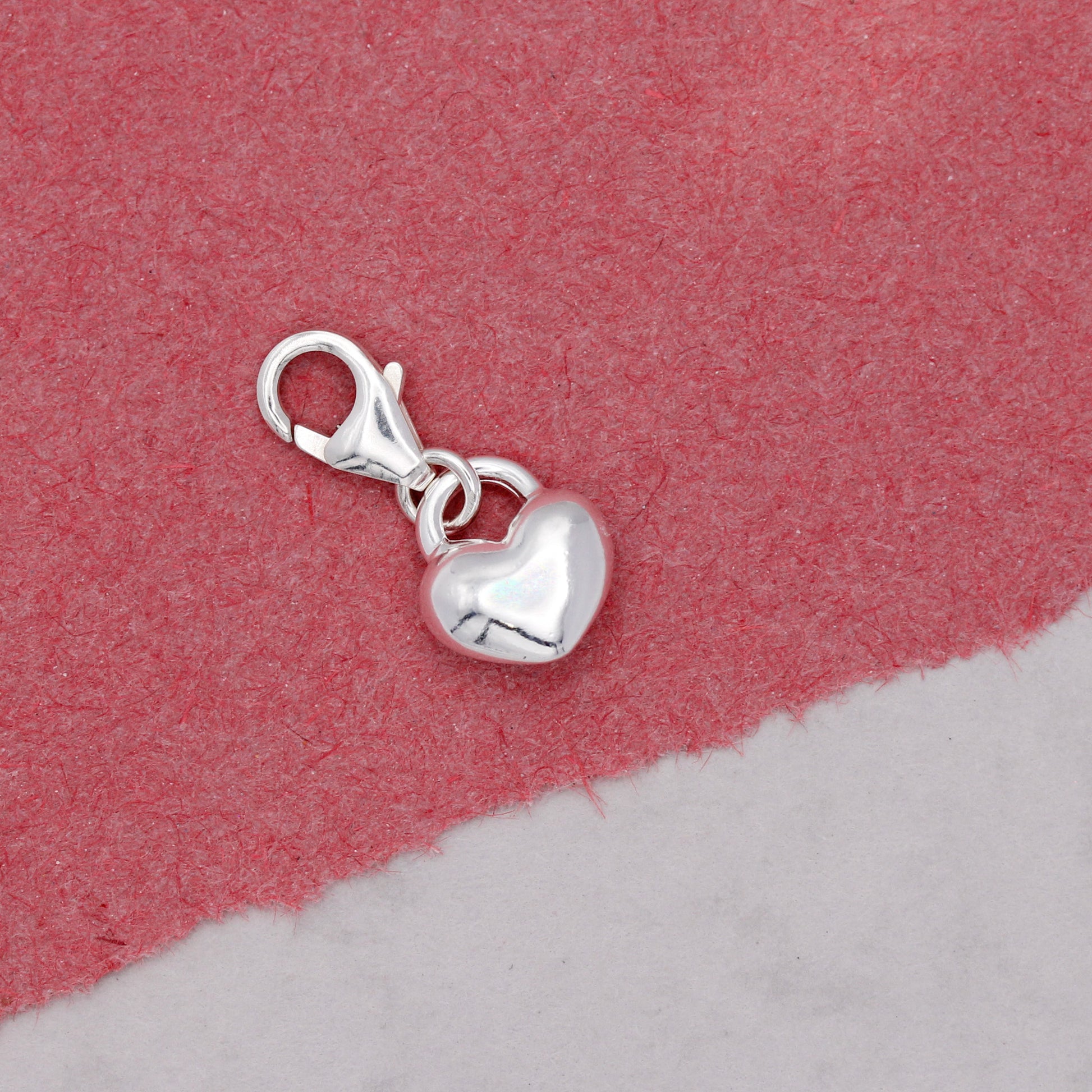 Silver heart-shaped charm with a clasp on a pink and gray background