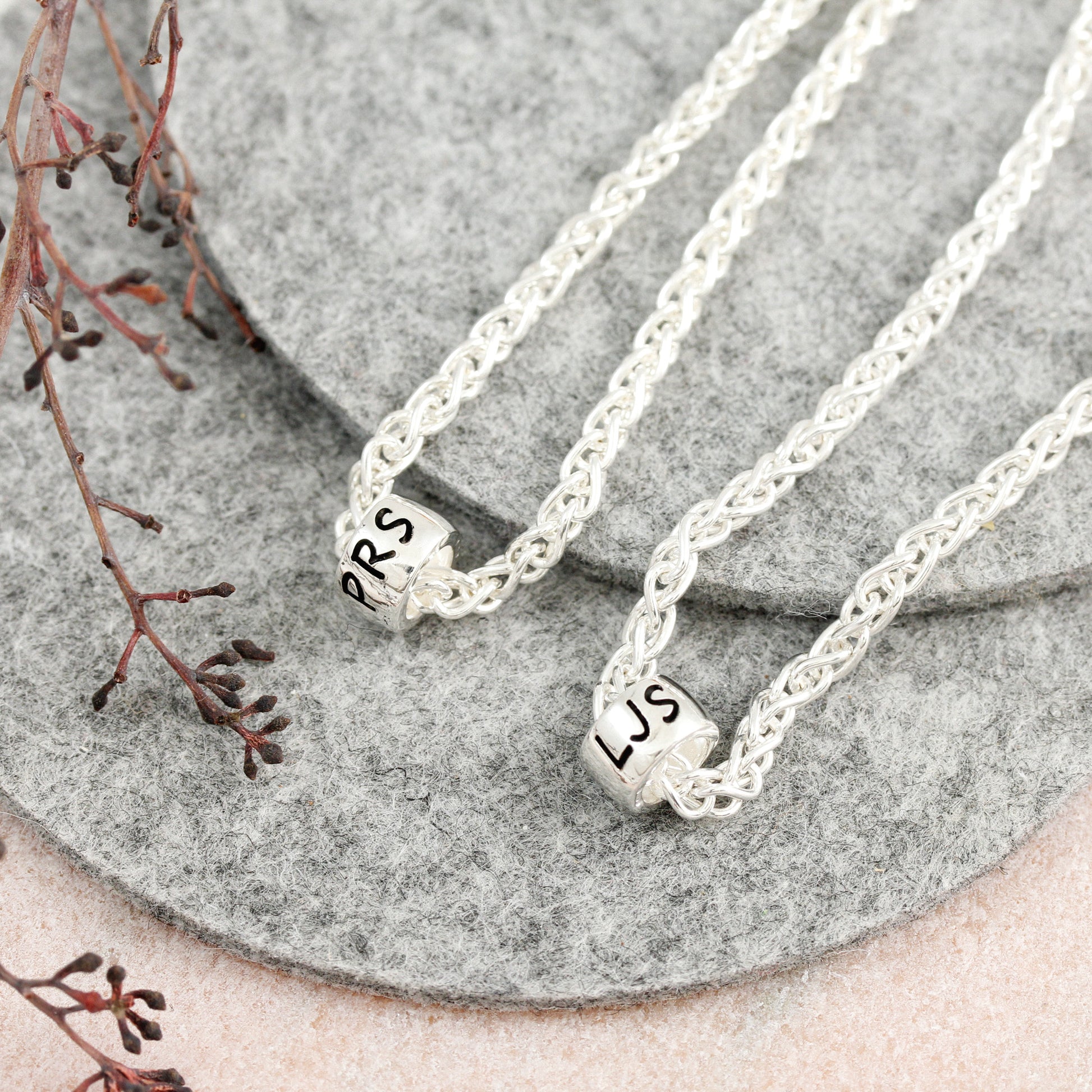 Two silver bracelets with engraved initials on a stone surface.