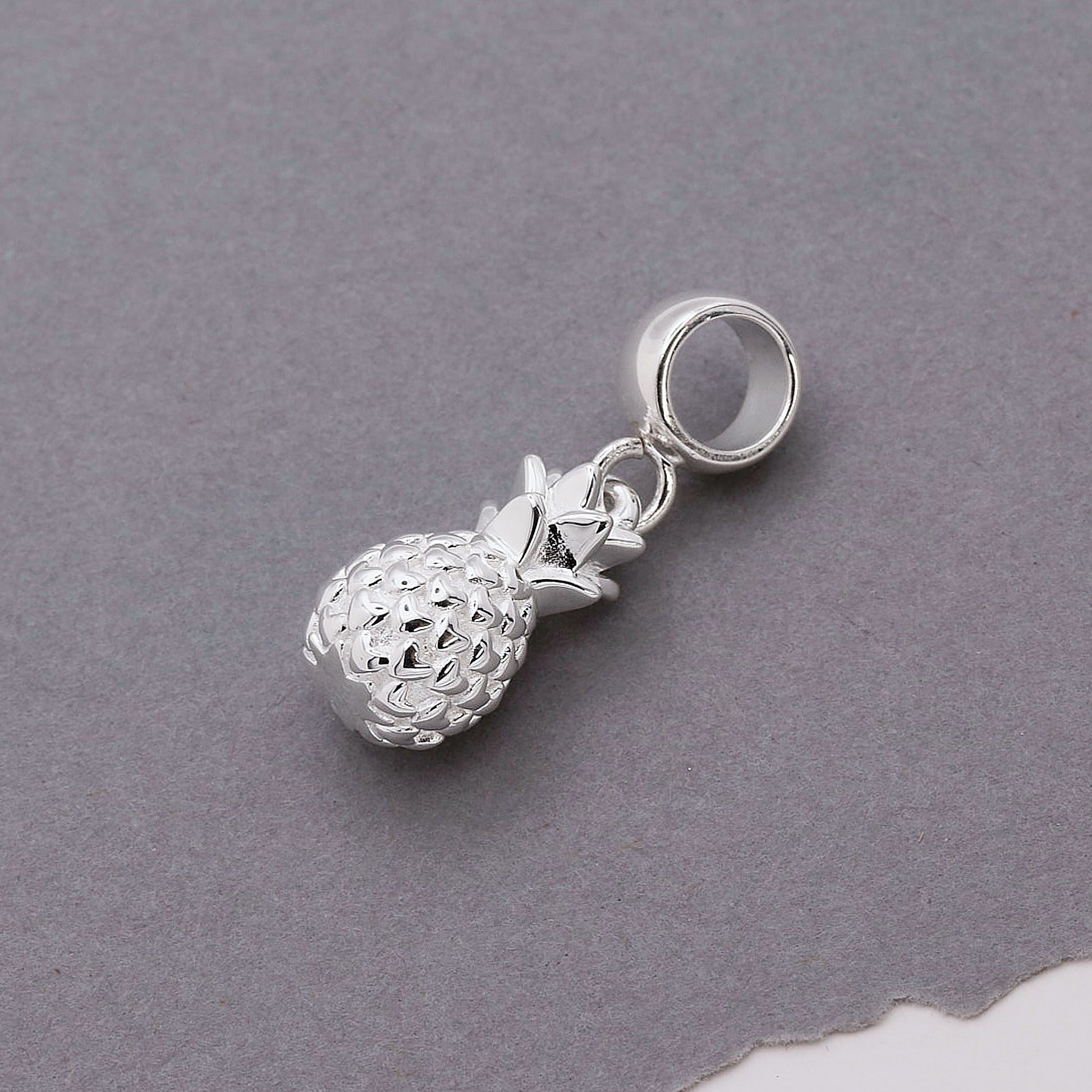Silver pineapple charm on a gray background