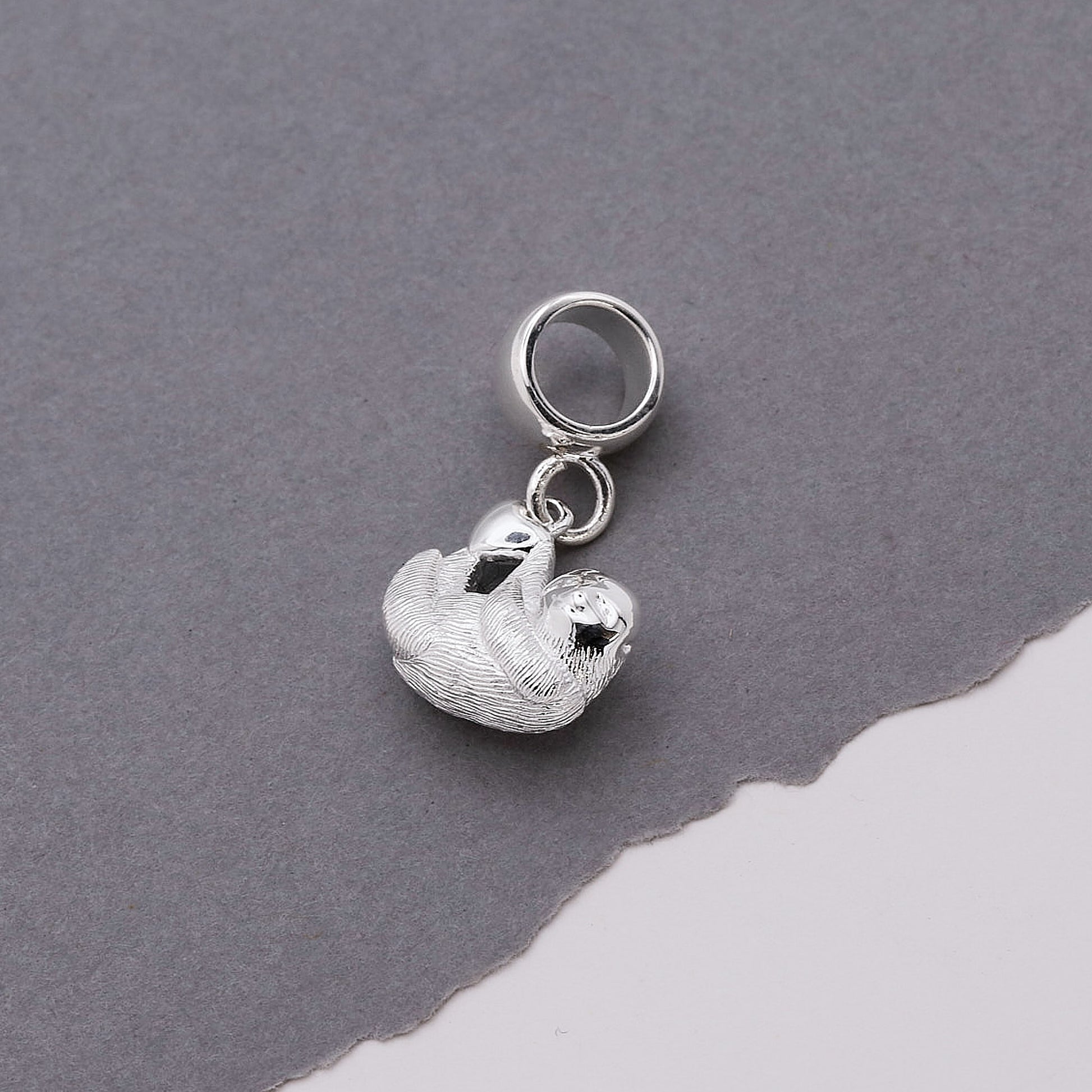 Silver sloth charm on a gray background