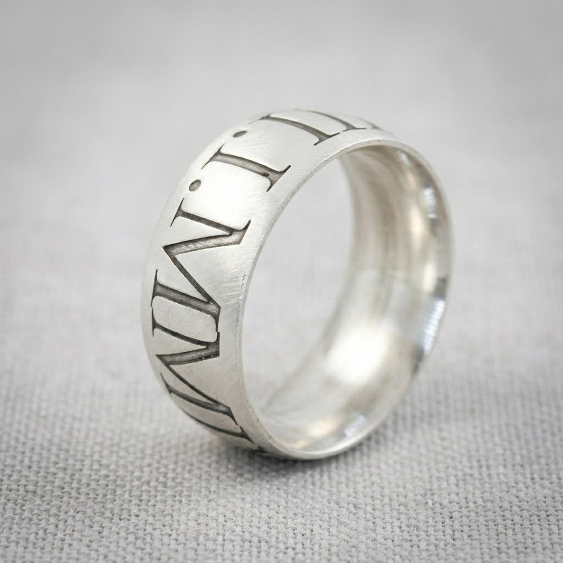 Silver ring with engraved design on a gray fabric background