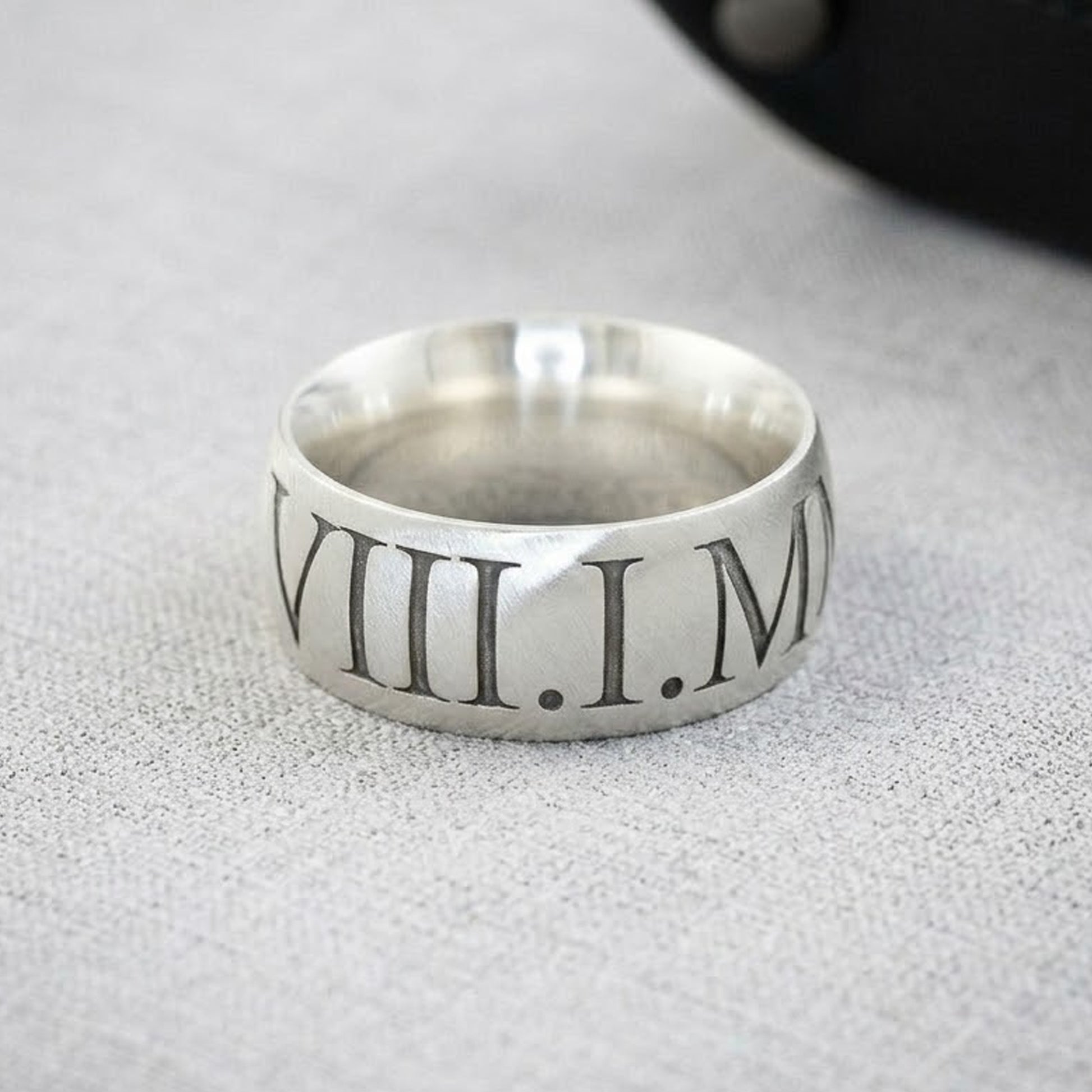 Silver ring with Roman numerals on a textured surface