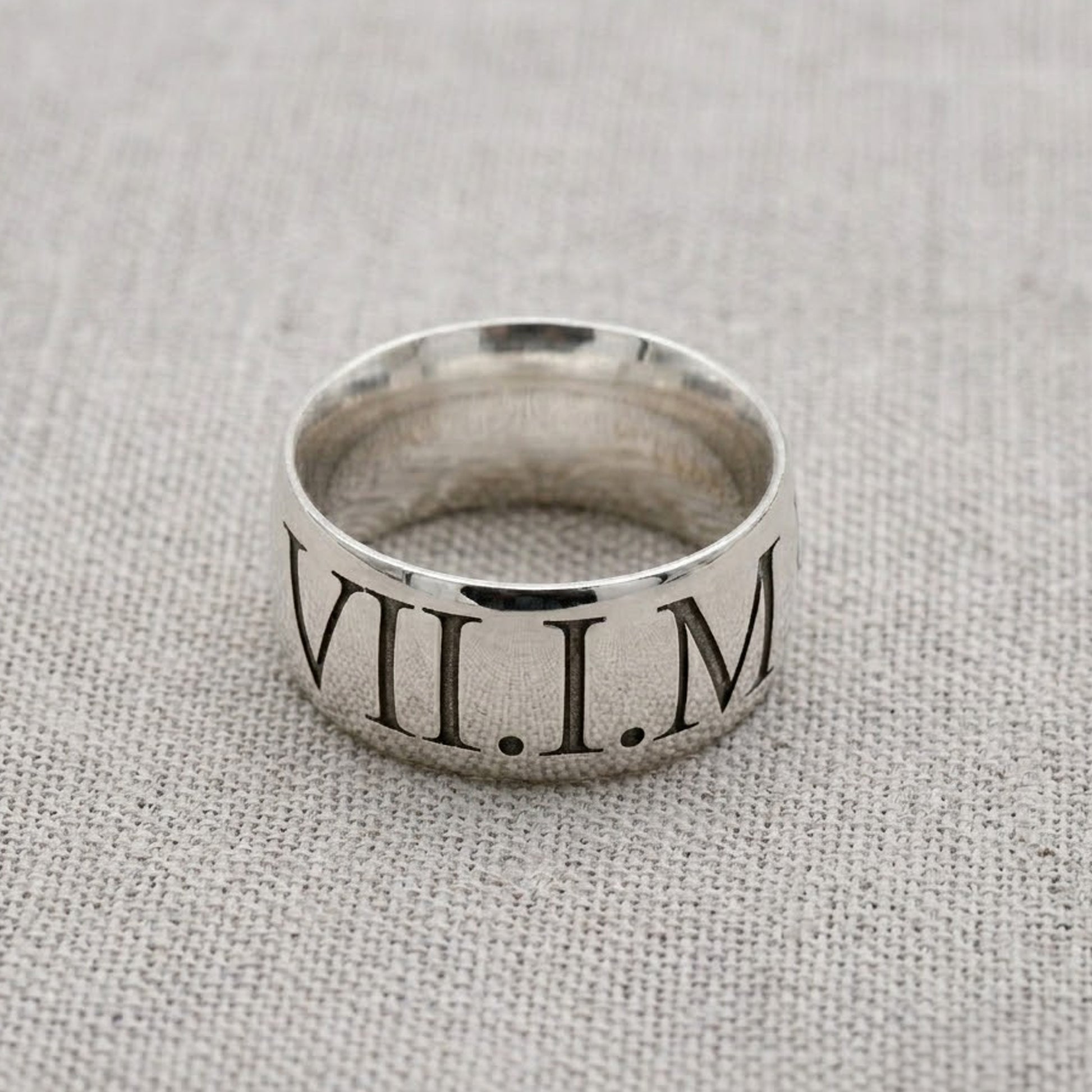 Silver ring with Roman numeral engraving on a textured fabric background