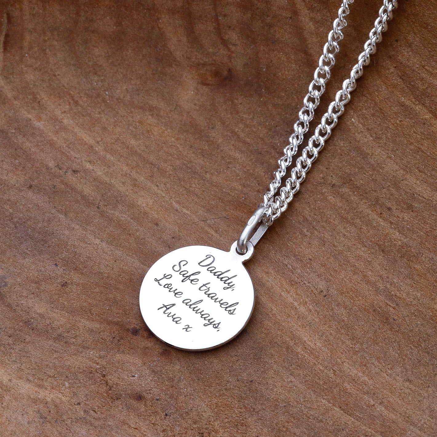 engraved back of silver saint christopher necklace on silver curb chain on wood surface