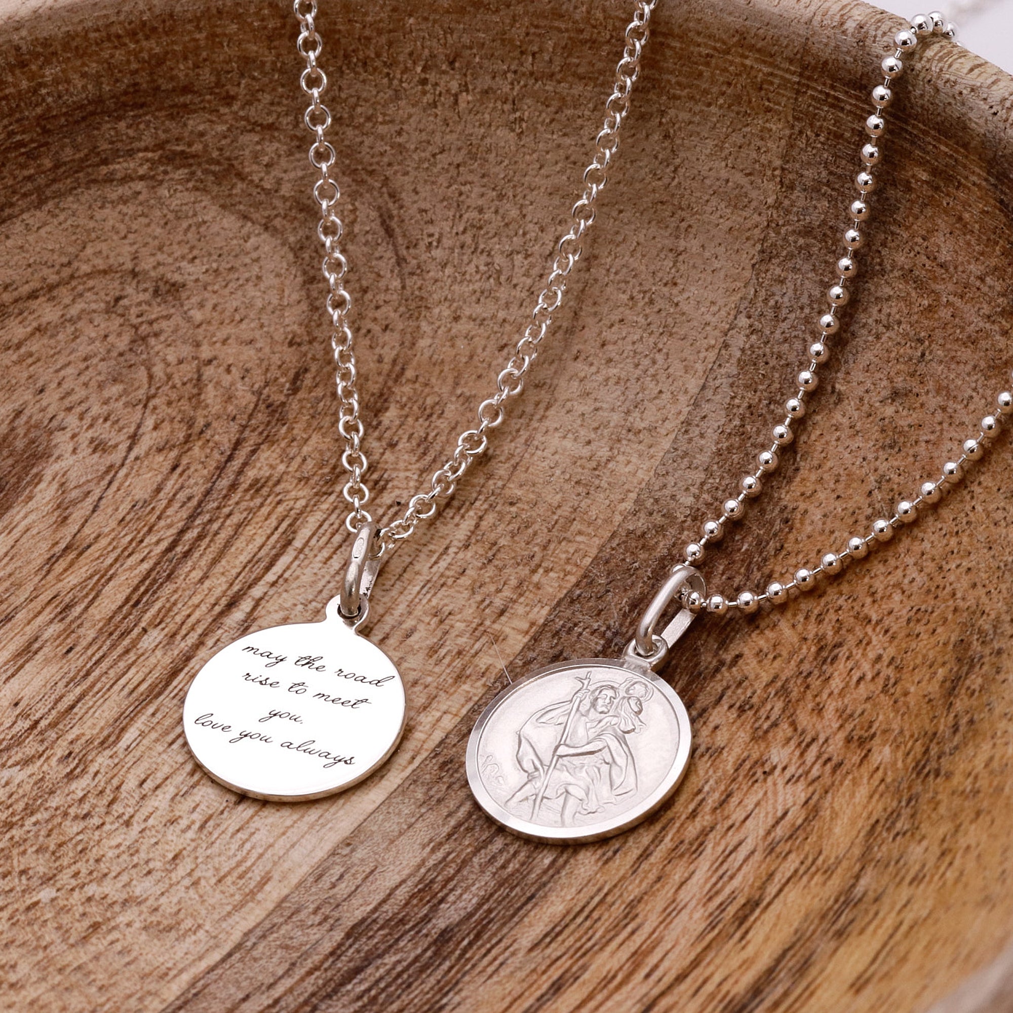 Two silver necklaces with engraved pendants on a wooden surface