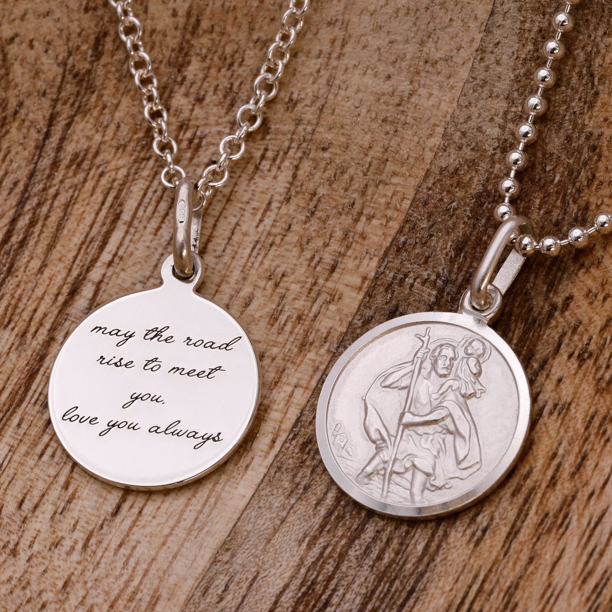 Two silver St Christopher pendants on a wooden surface