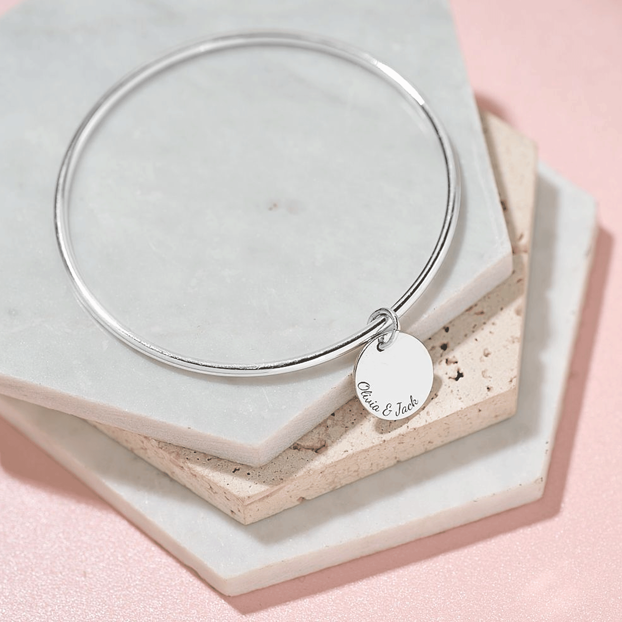 Silver bangle with engraved names on a tag on a marble surface
