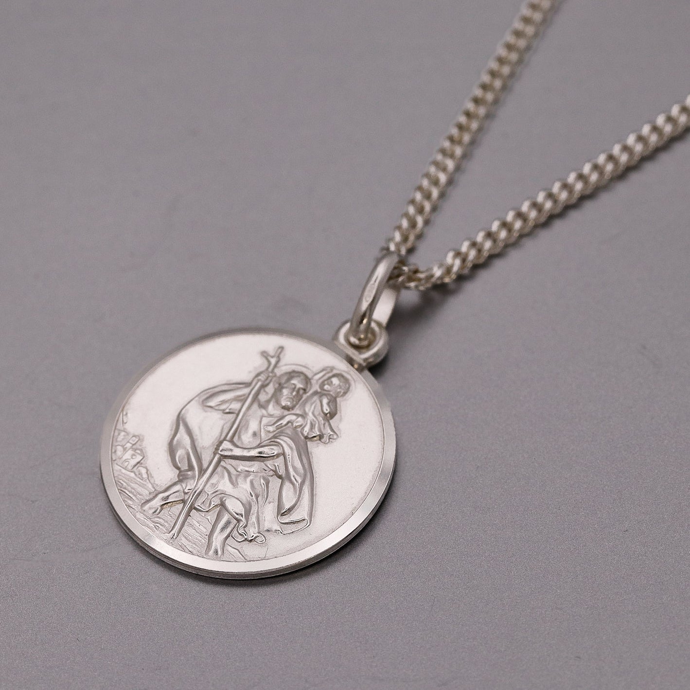 Silver necklace with a round pendant featuring an engraved design on a gray background