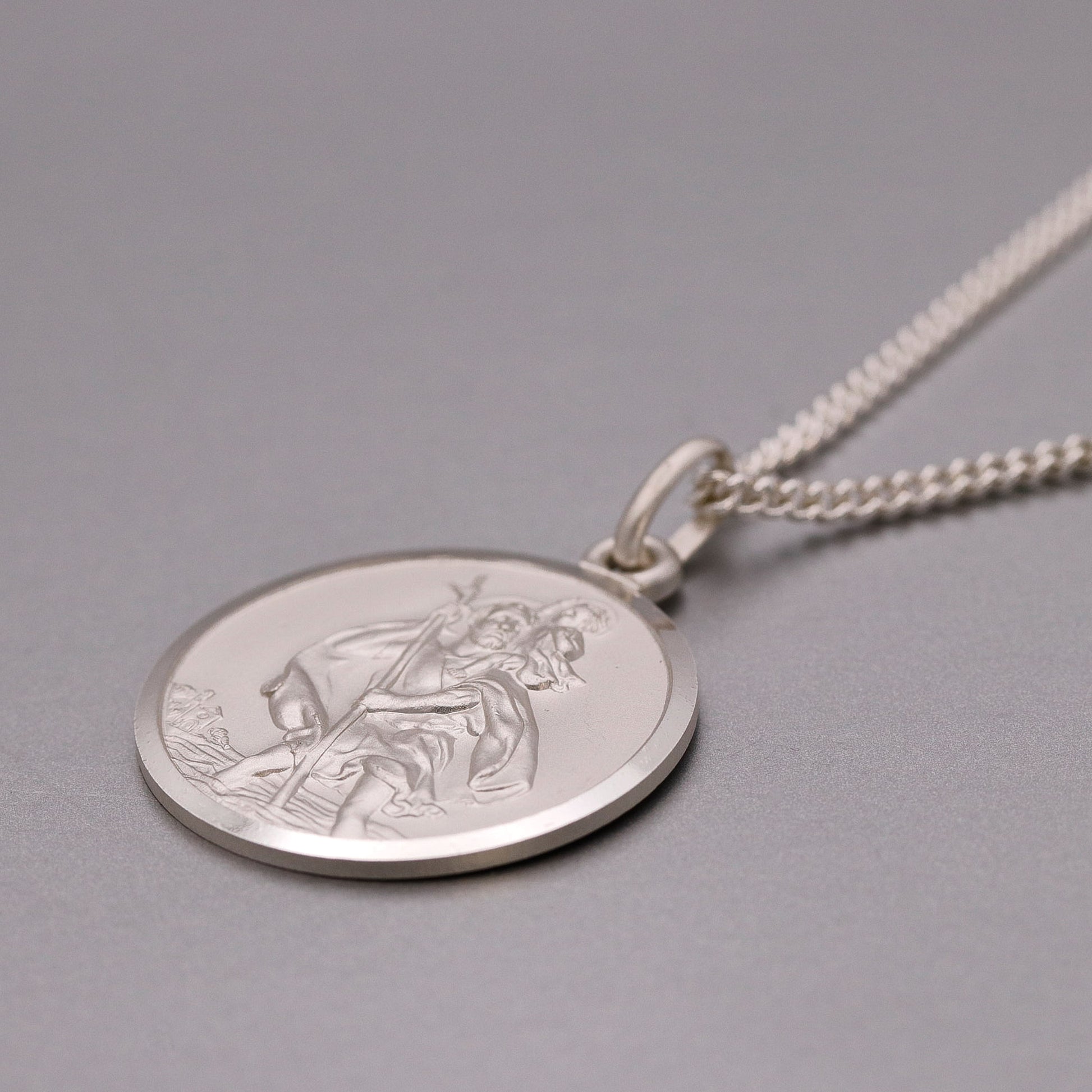 Silver St Christopher necklace with a round pendant featuring an engraved design on a gray background