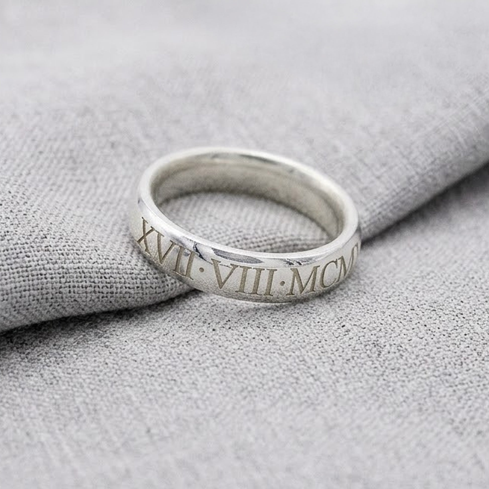 Silver ring with Roman numerals on a textured gray surface
