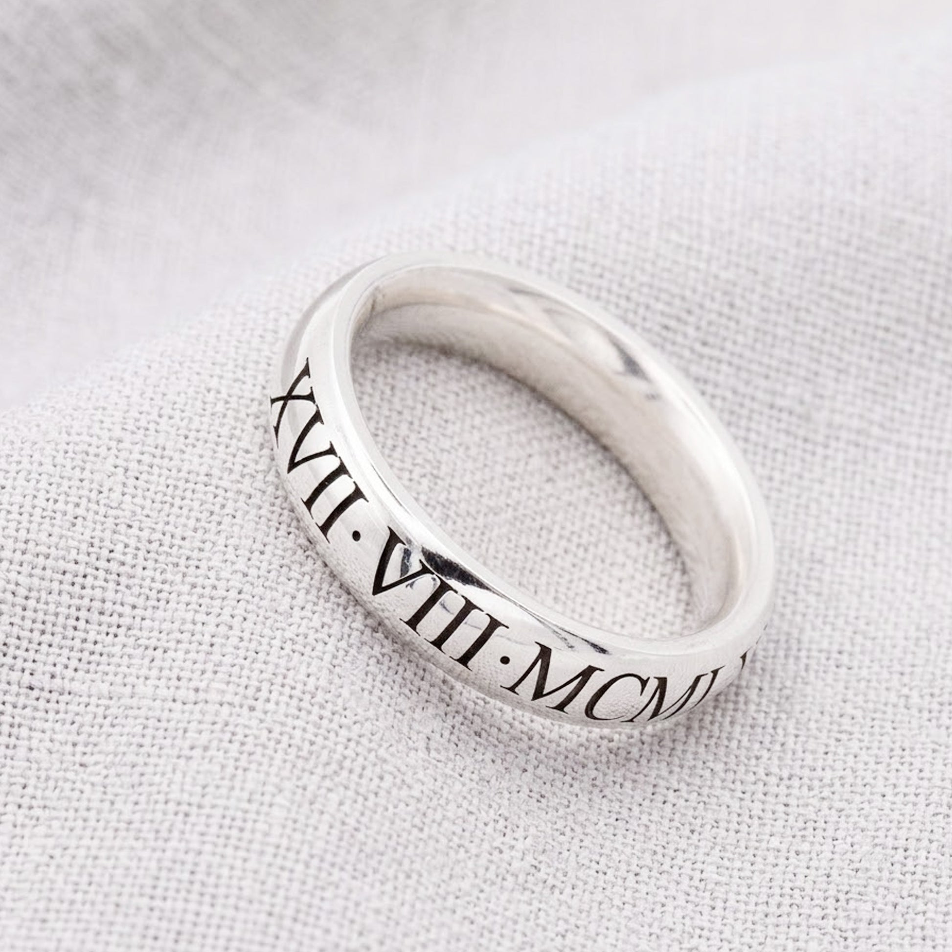 Silver ring with Roman numerals on a light fabric background