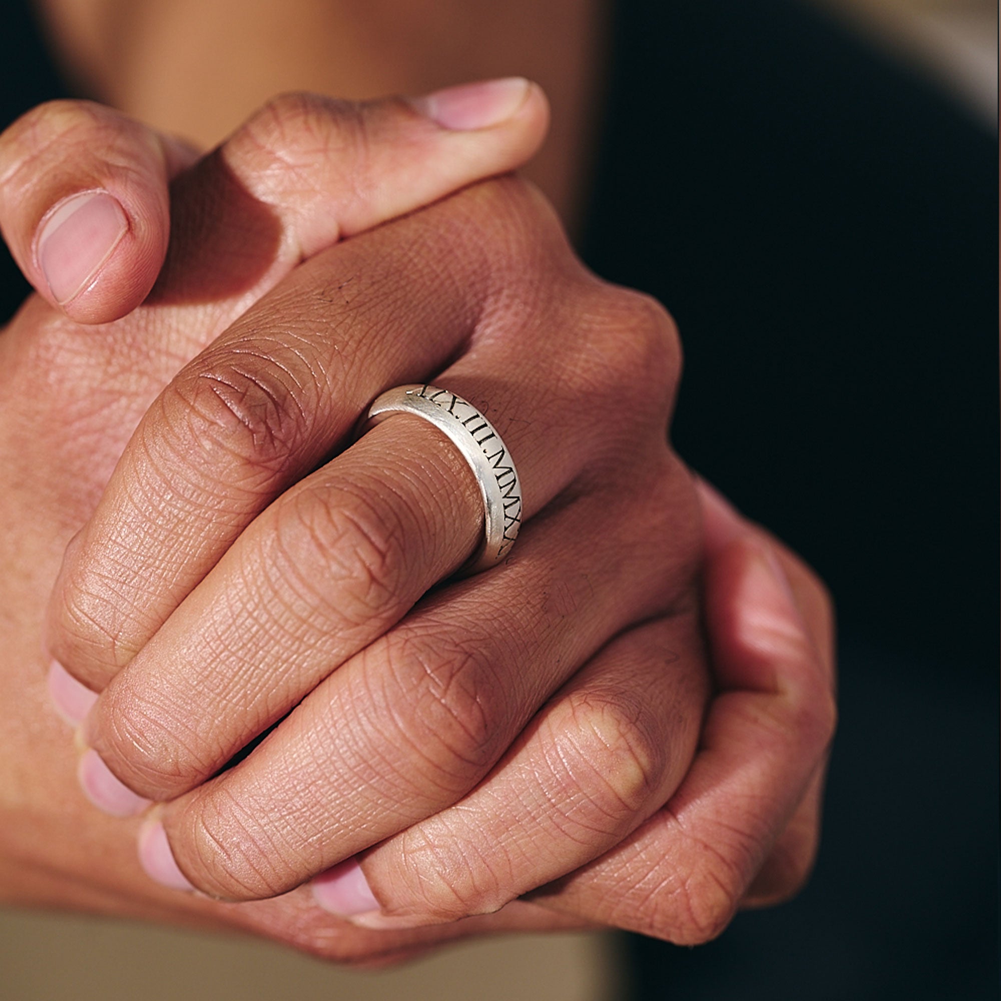 Close-up of a hand wearing a silver ring with engraved text, against a blurred background.