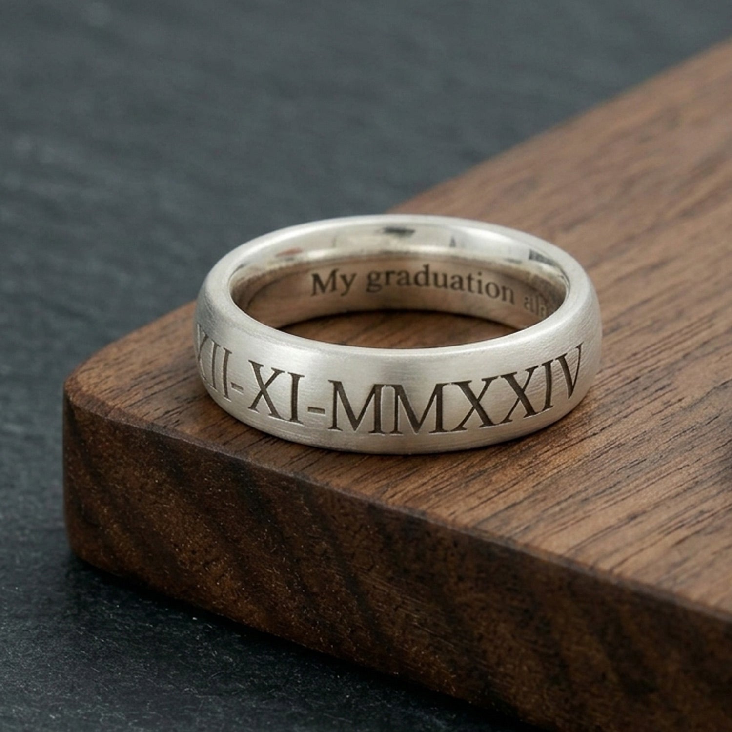 Silver ring with Roman numerals and engraved text on a wooden surface