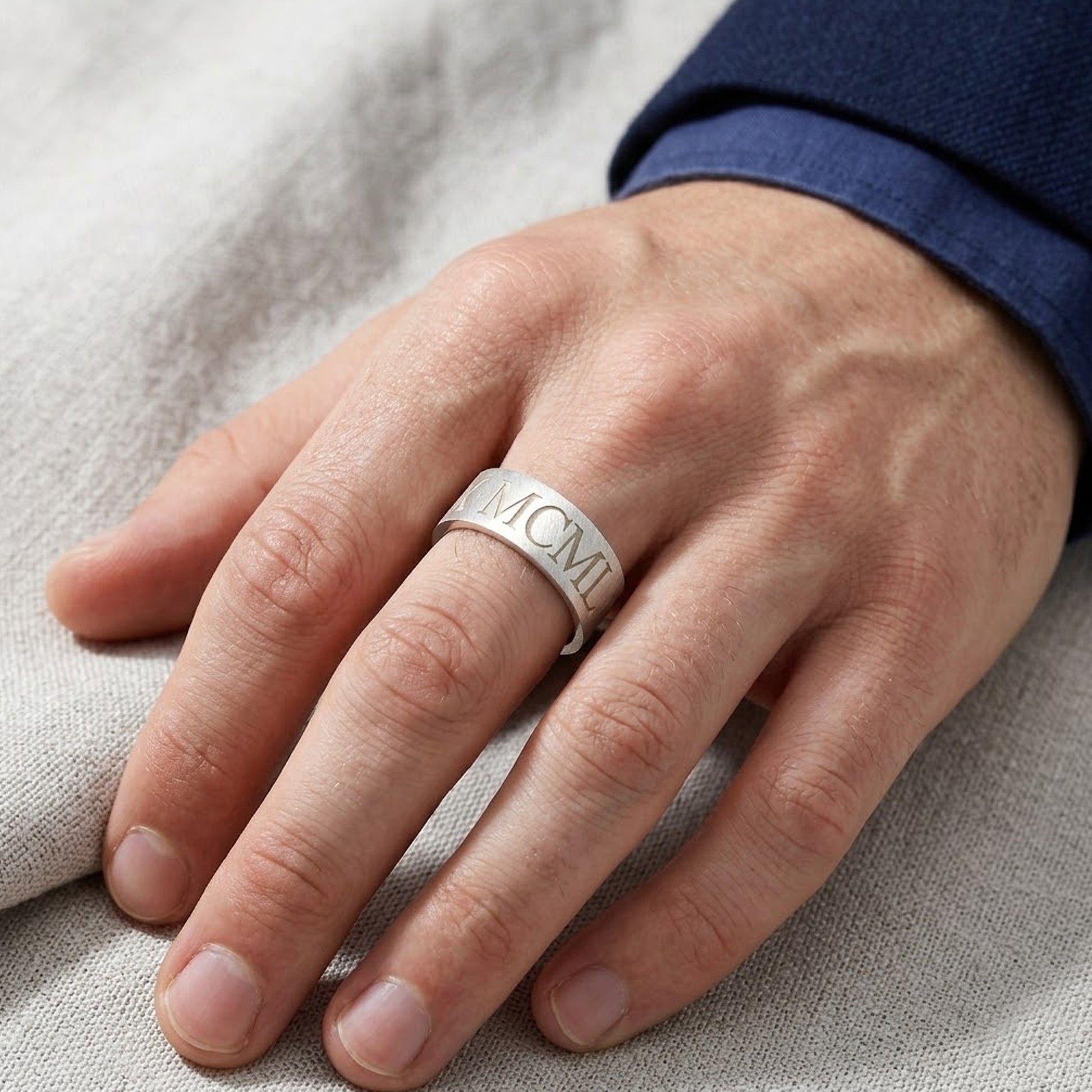 Hand wearing a silver ring with 'MCM' engraving on a neutral background