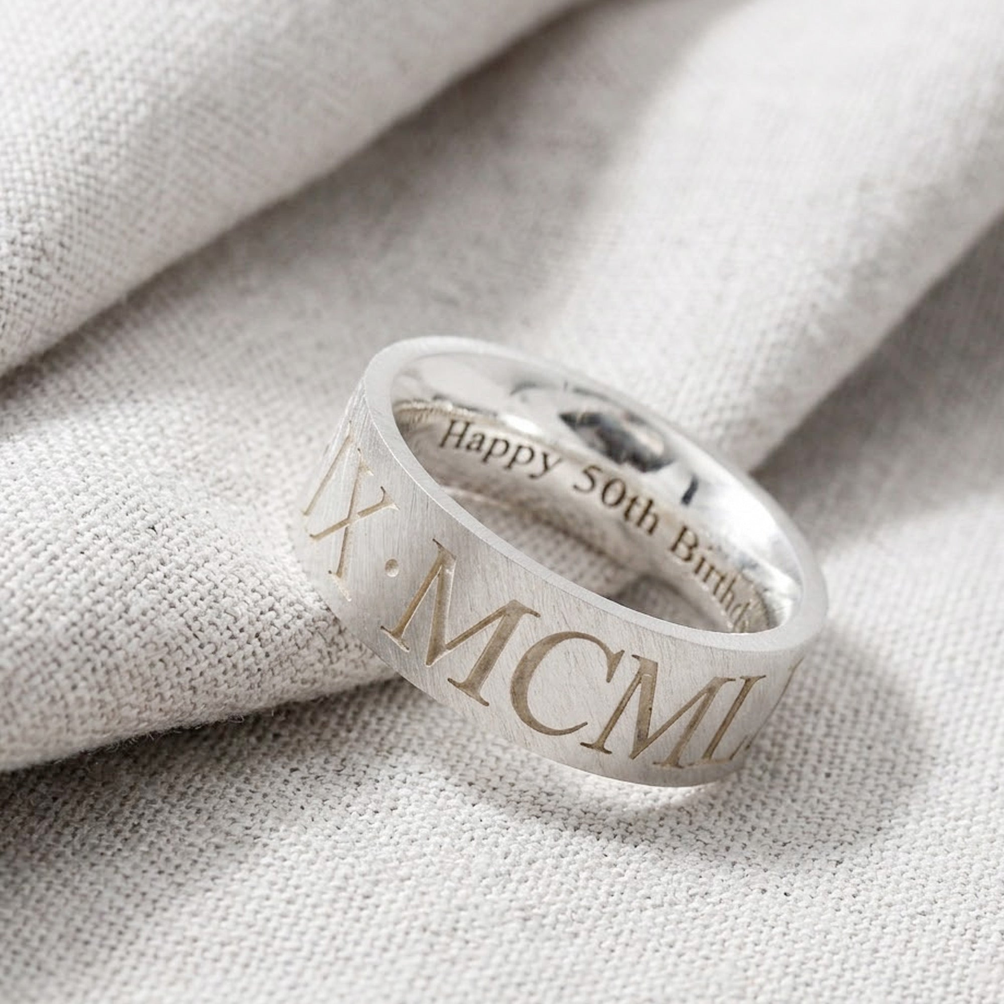 Silver ring with Roman numeral engraving on a textured fabric background