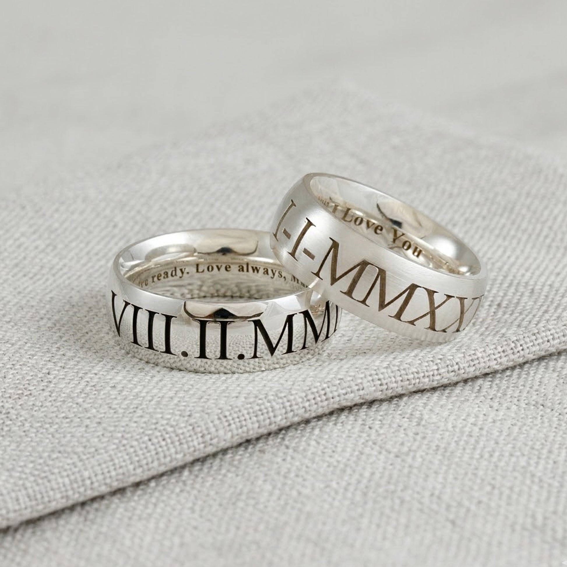 Two silver rings with Roman numeral inscriptions on a textured gray surface