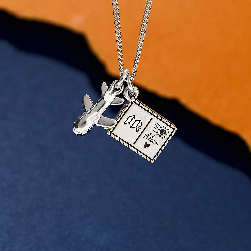 Silver necklace with airplane and card charm on a blue and orange gradient background