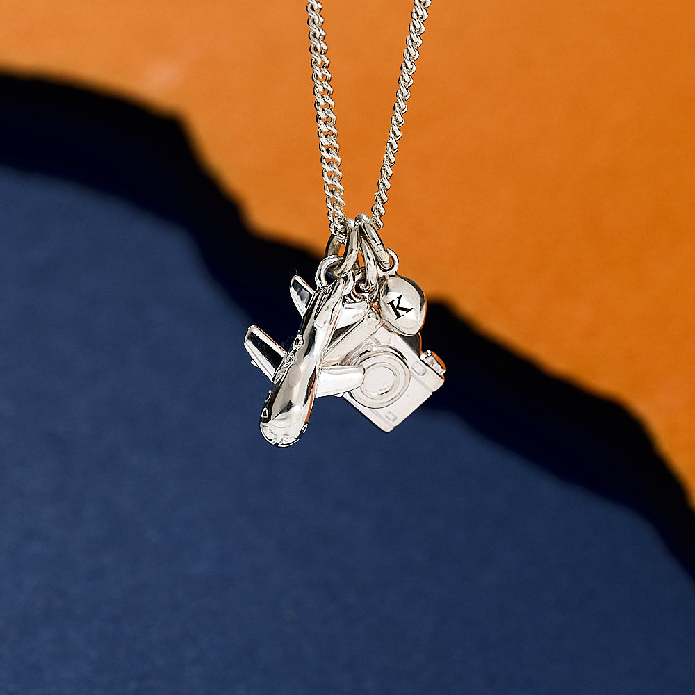 Silver necklace with airplane and camera charms on a blue and orange gradient background