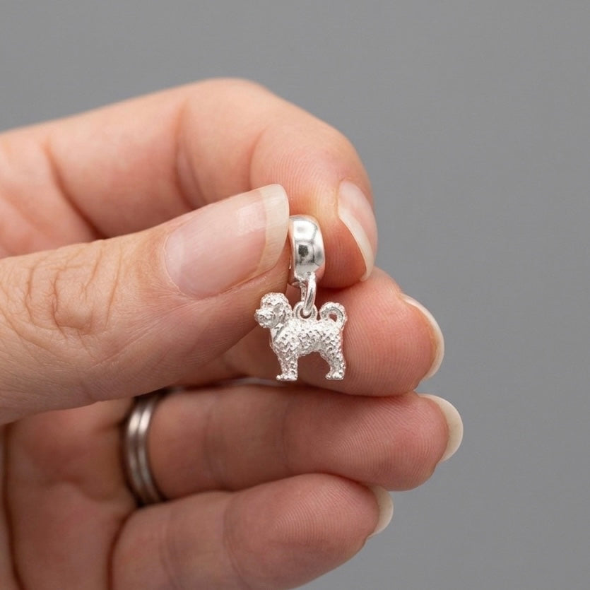 A silver dog charm pendant held between fingers to show its small scale, set against a solid gray background.