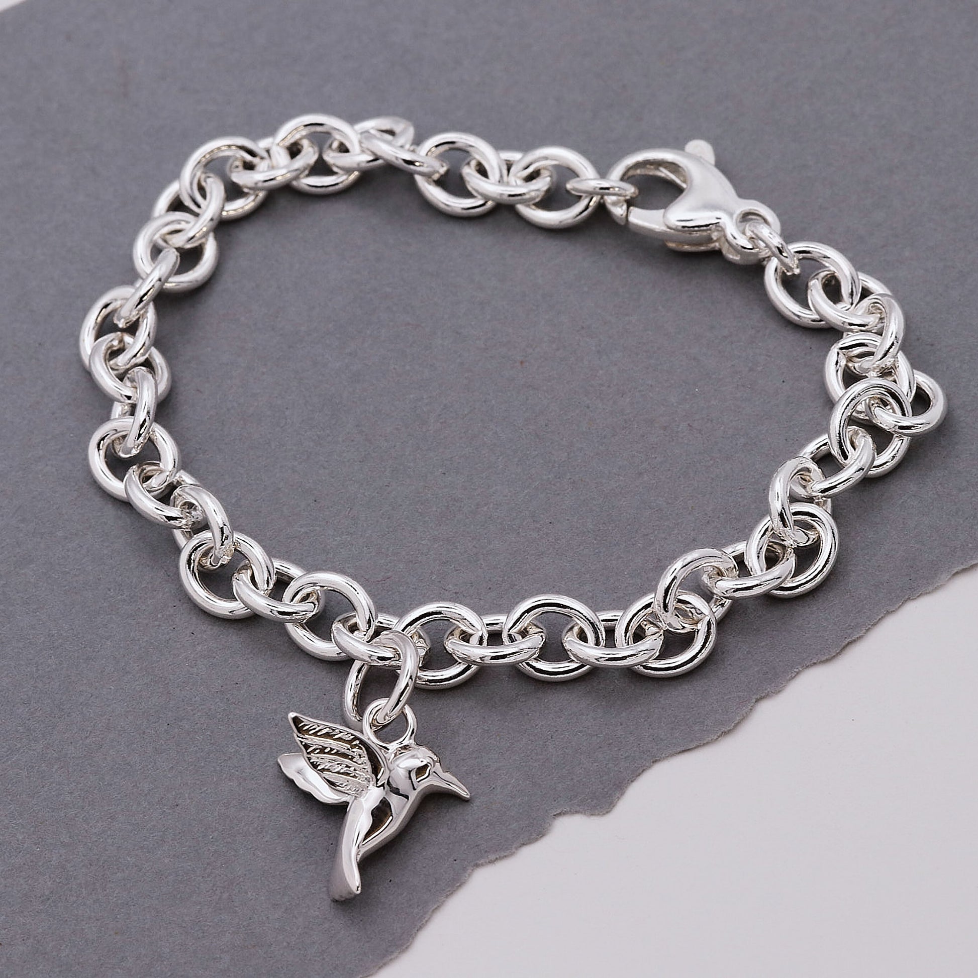 Silver chain bracelet with a hummingbird charm on a gray background