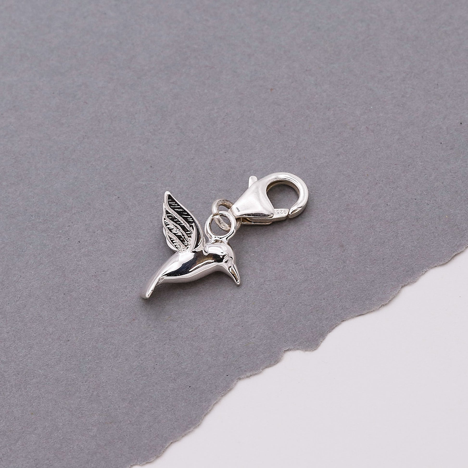Silver hummingbird charm on a gray background