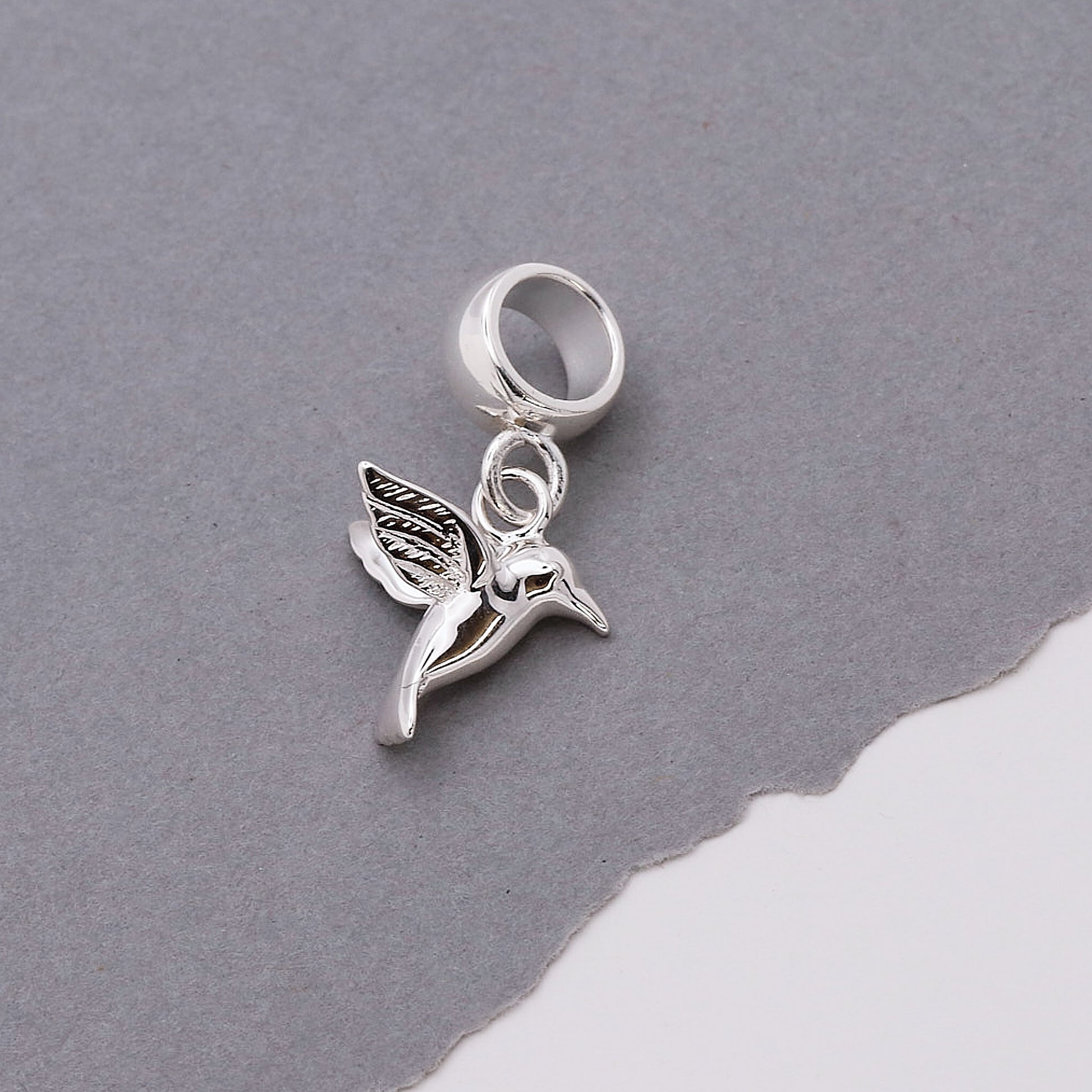 Silver hummingbird charm on a gray background