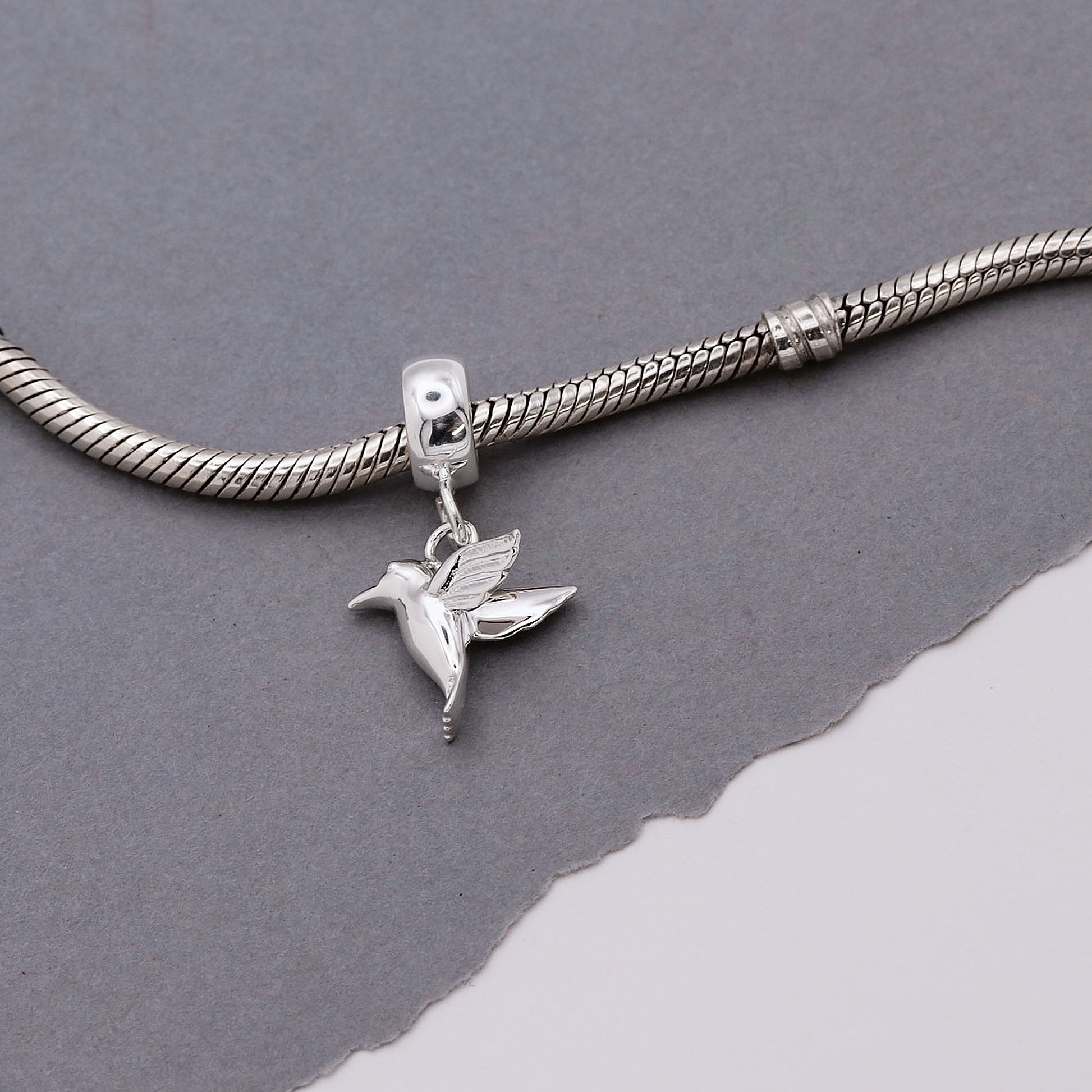 Silver bracelet with a hummingbird charm on a gray background