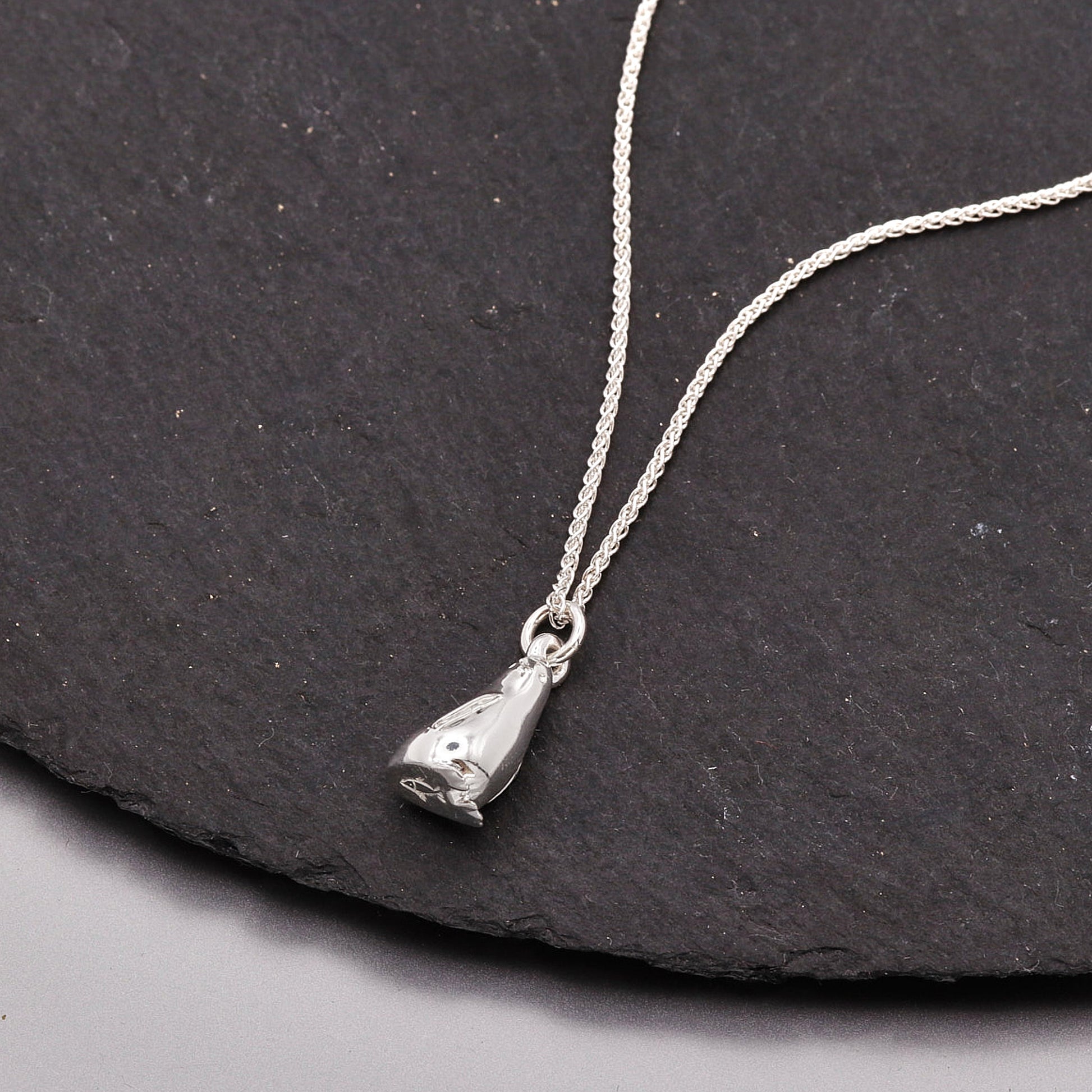 Silver penguin necklace with a pendant on a dark stone surface