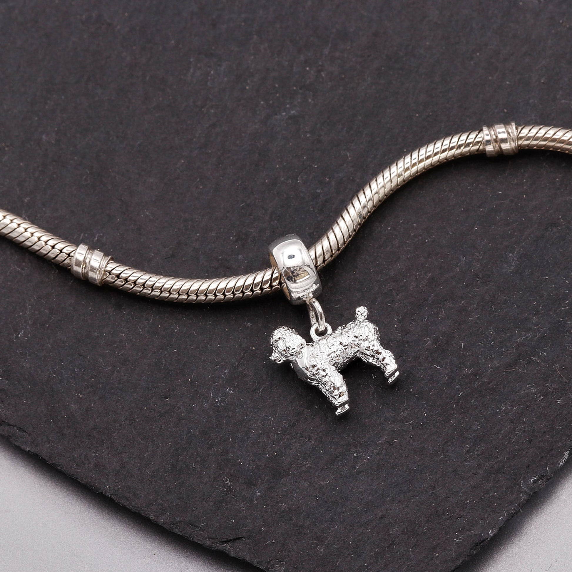 Silver snake chain bracelet with a dog charm on a dark stone surface