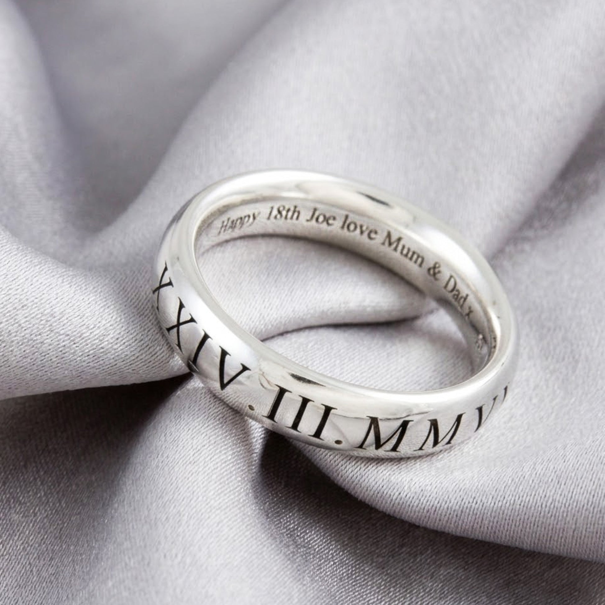 Silver ring with engraved text on a gray fabric background