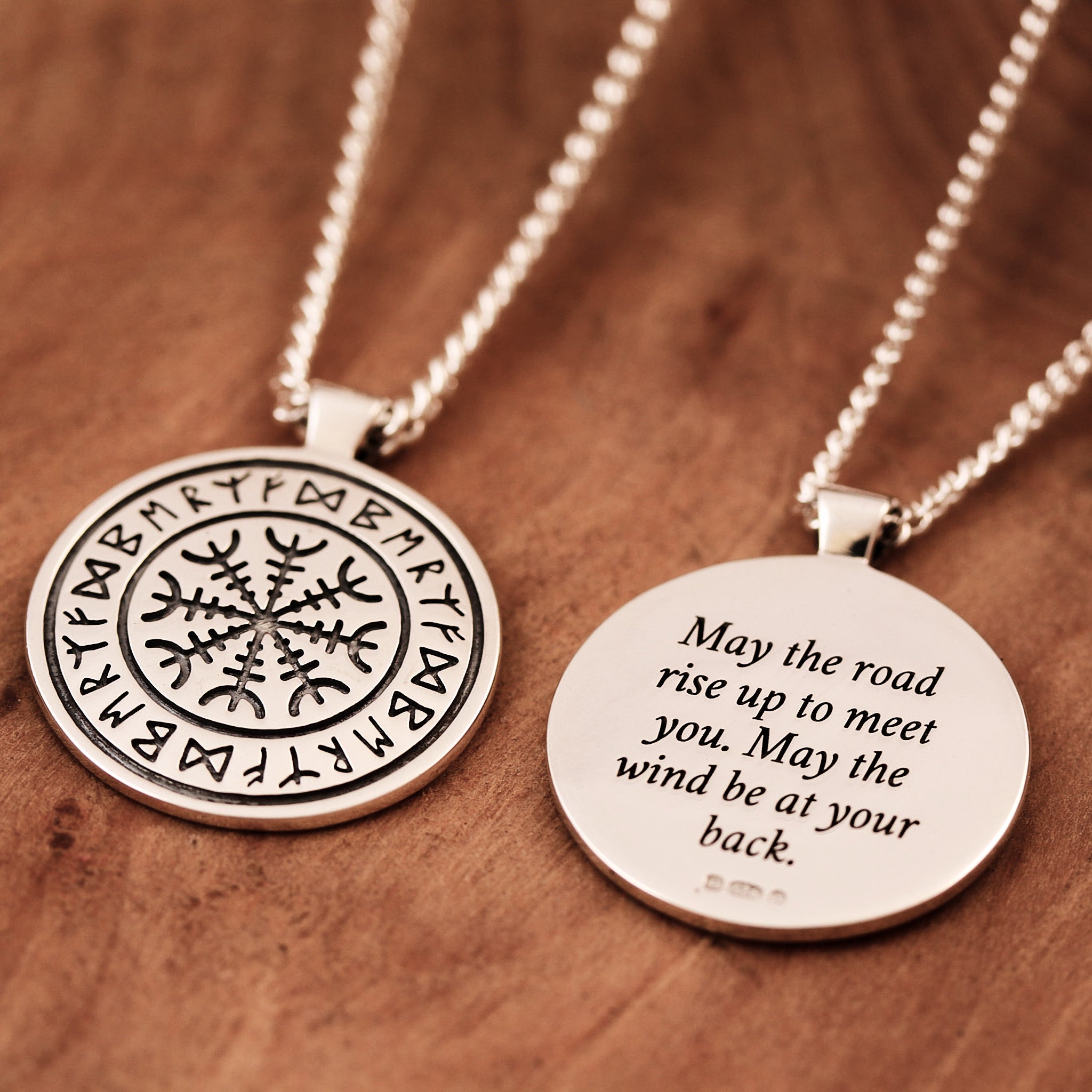 Two silver necklaces with engraved viking rune designs on a wooden surface