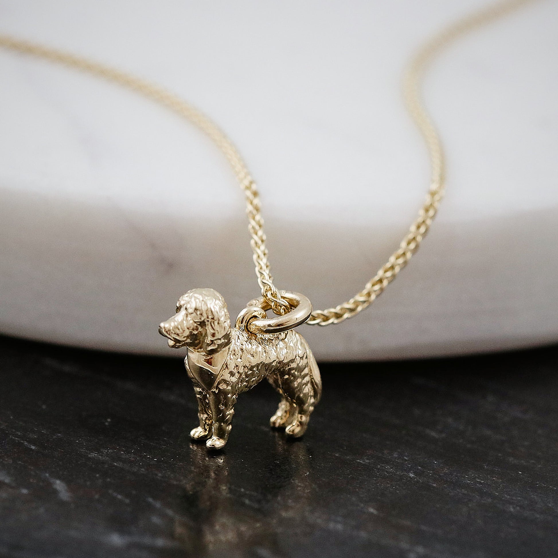 Gold labradoodle dog-shaped pendant on a chain against a white and black background