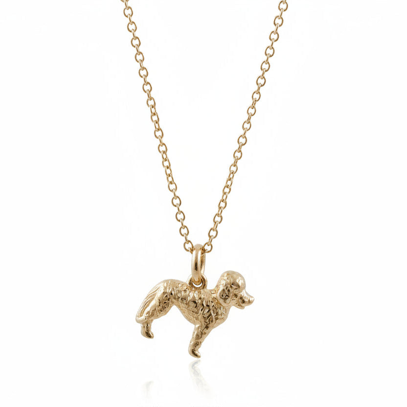 Gold labradoodle dog-shaped pendant on a chain against a white background