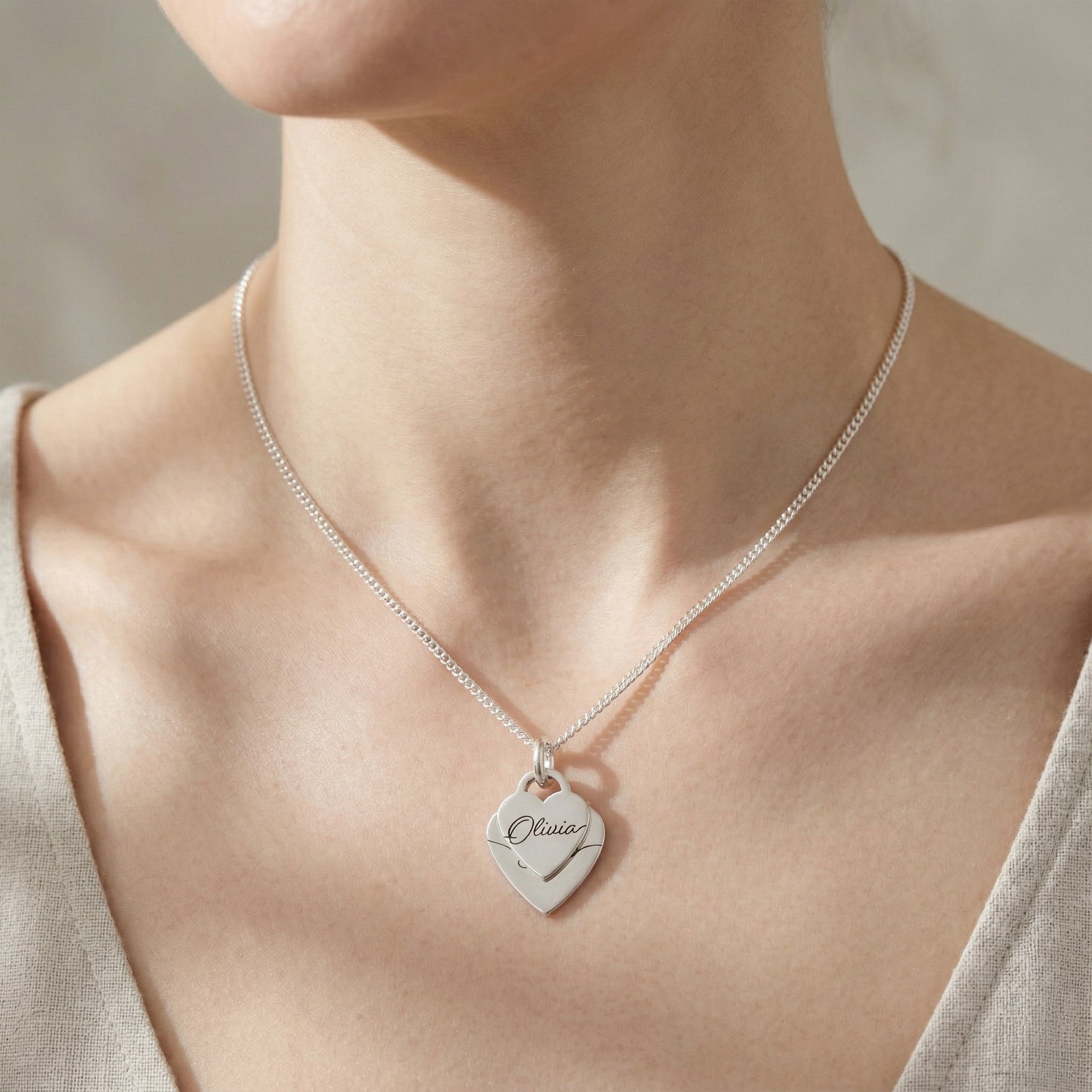Silver necklace with a heart-shaped pendant on a person wearing a beige top.