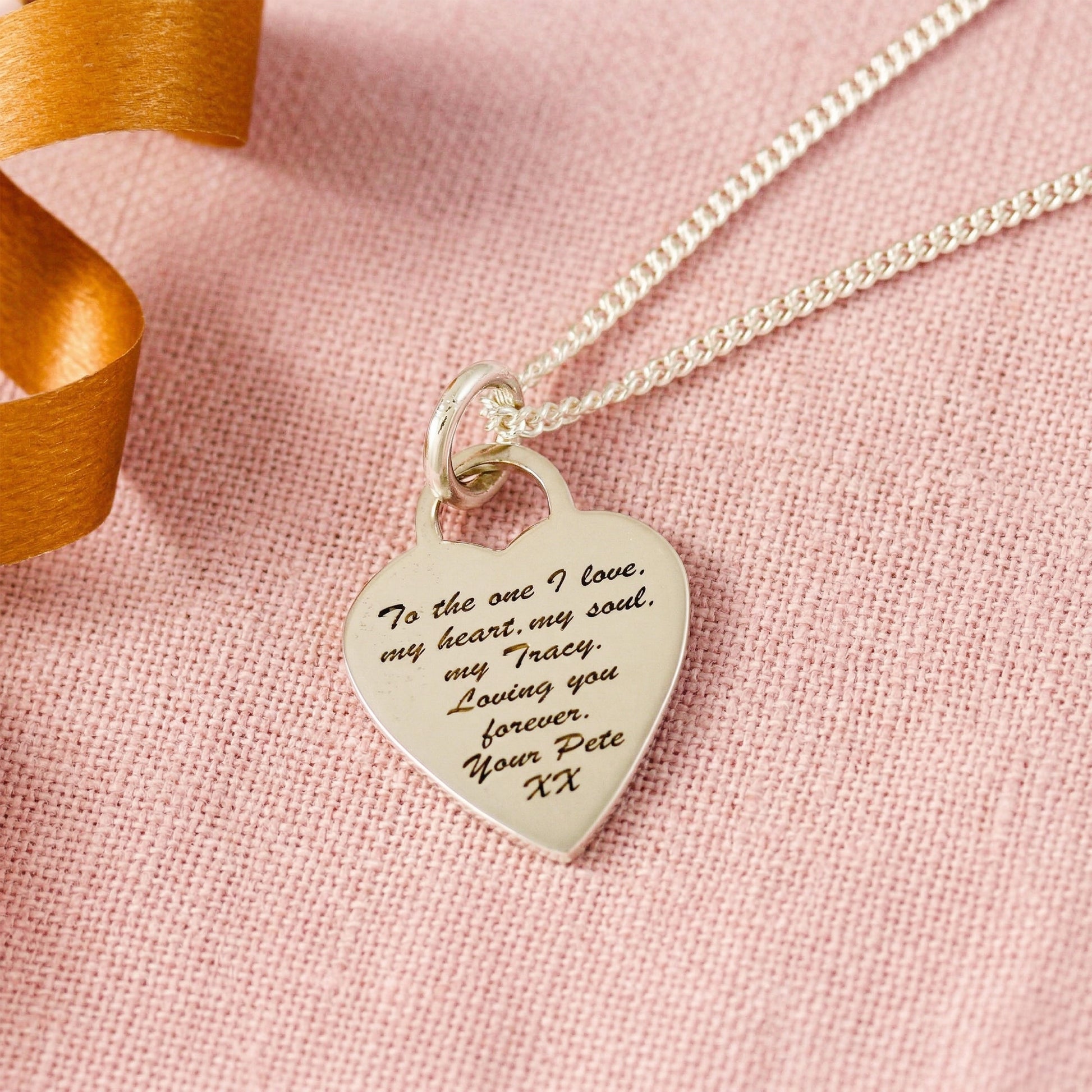Heart-shaped pendant necklace with engraved message on a pink fabric background