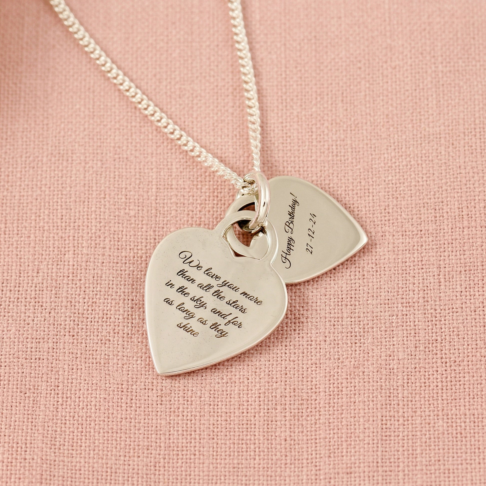Silver necklace with heart-shaped pendants on a pink background