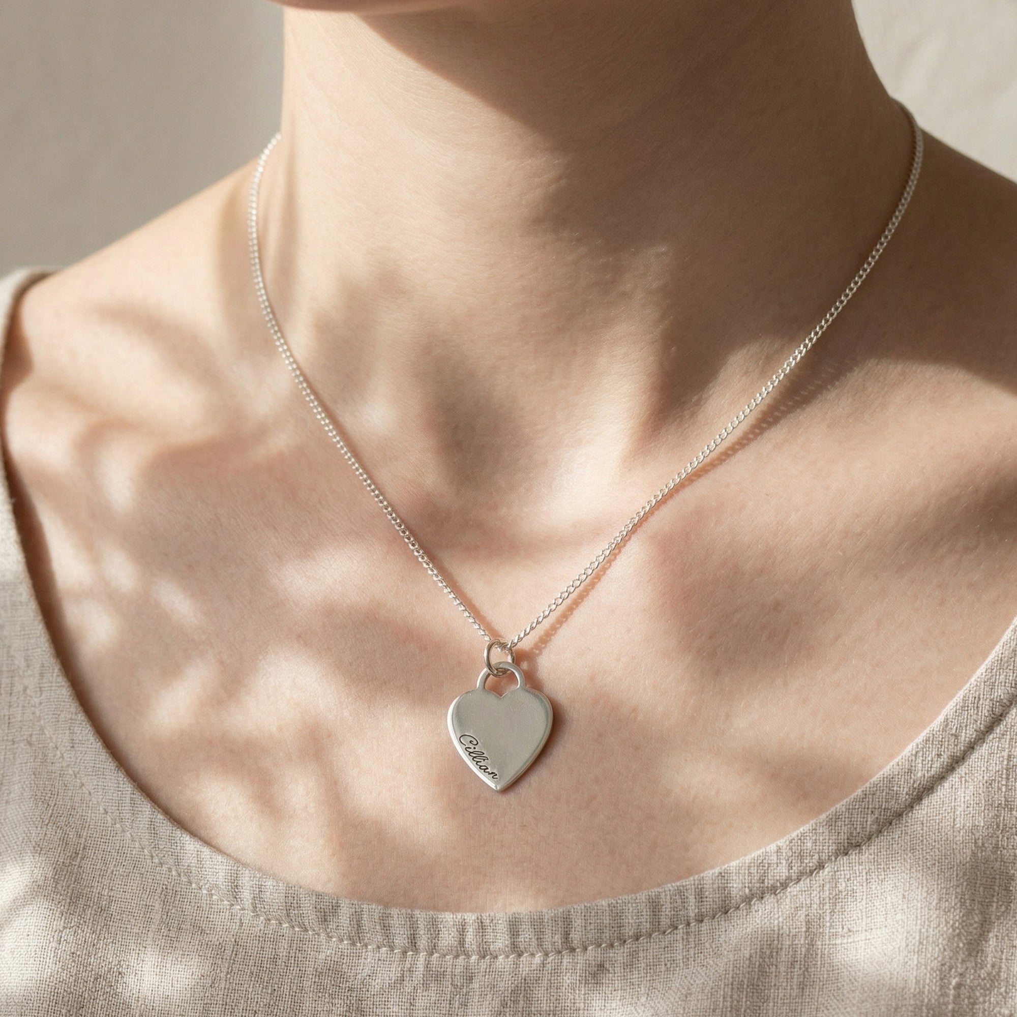 Person wearing a silver necklace with a heart-shaped pendant on a neutral background