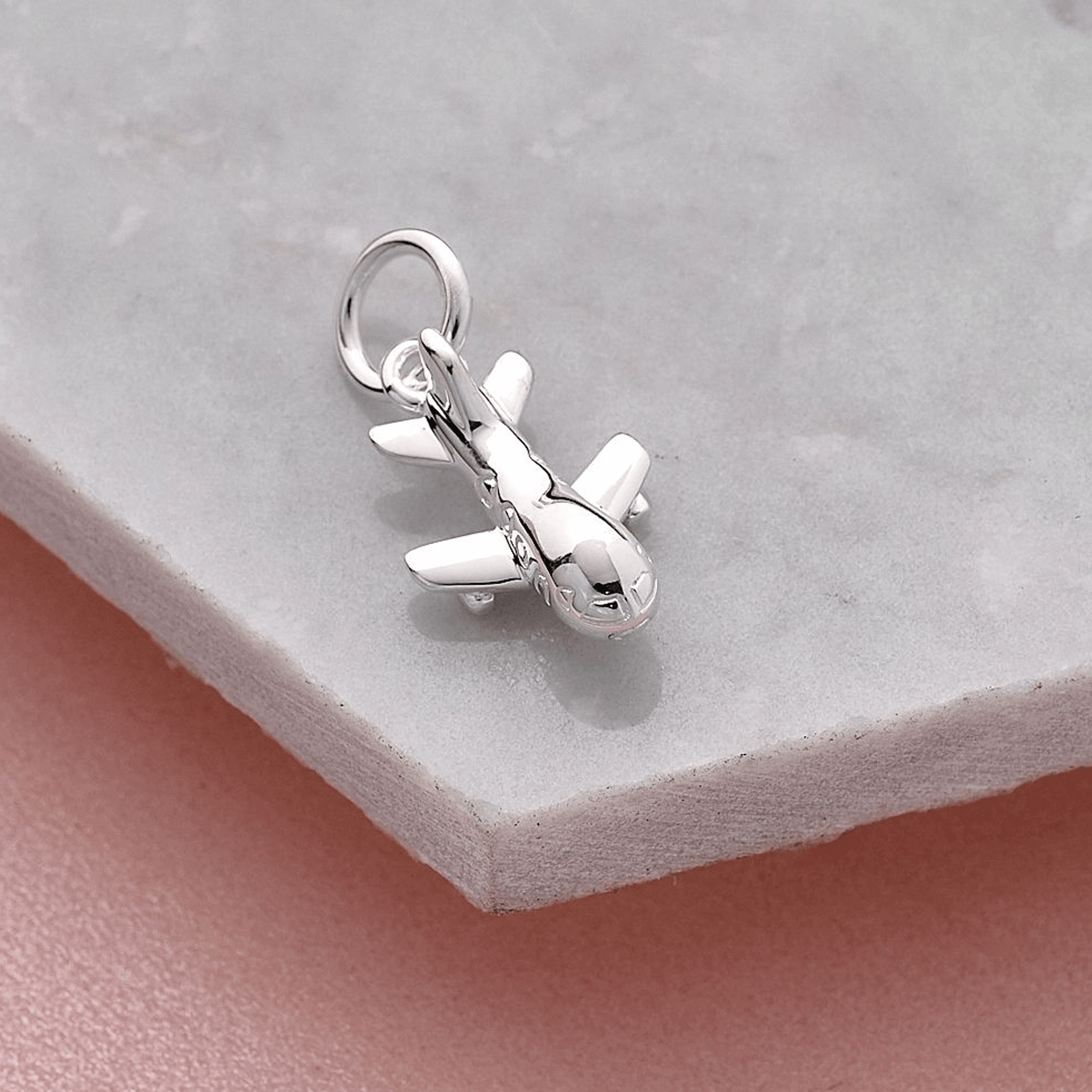 Silver airplane charm with a soldered jump ring on a grey stone surface