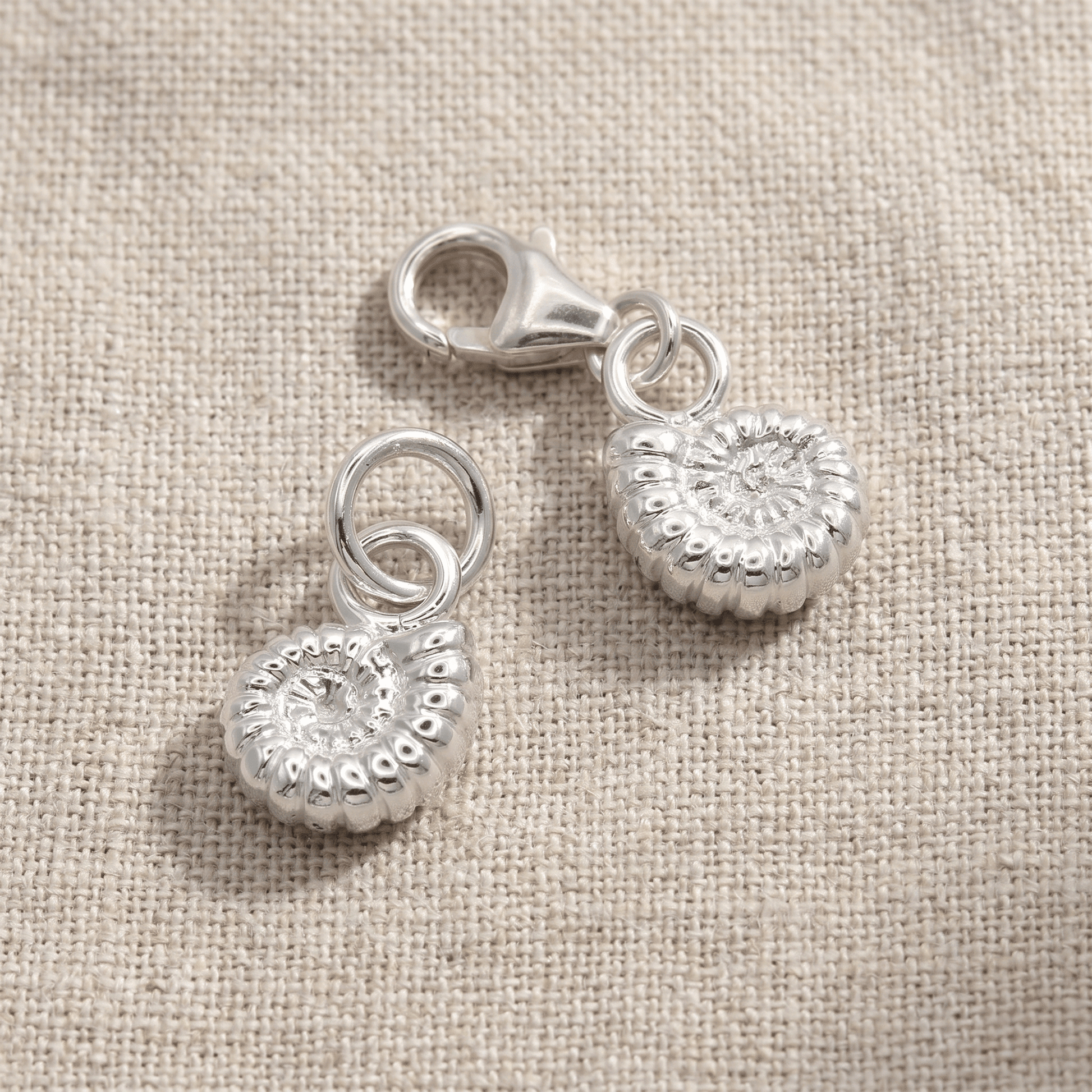 Two silver charms on a beige fabric background