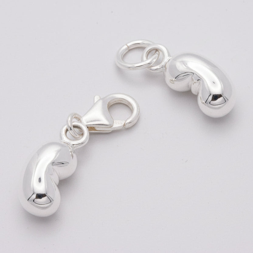 Two silver baby bean charms on a textured surface