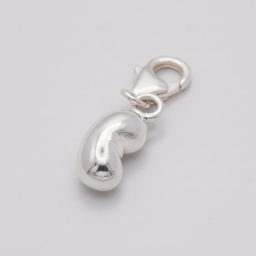 Silver charm shaped like a bean on a textured surface