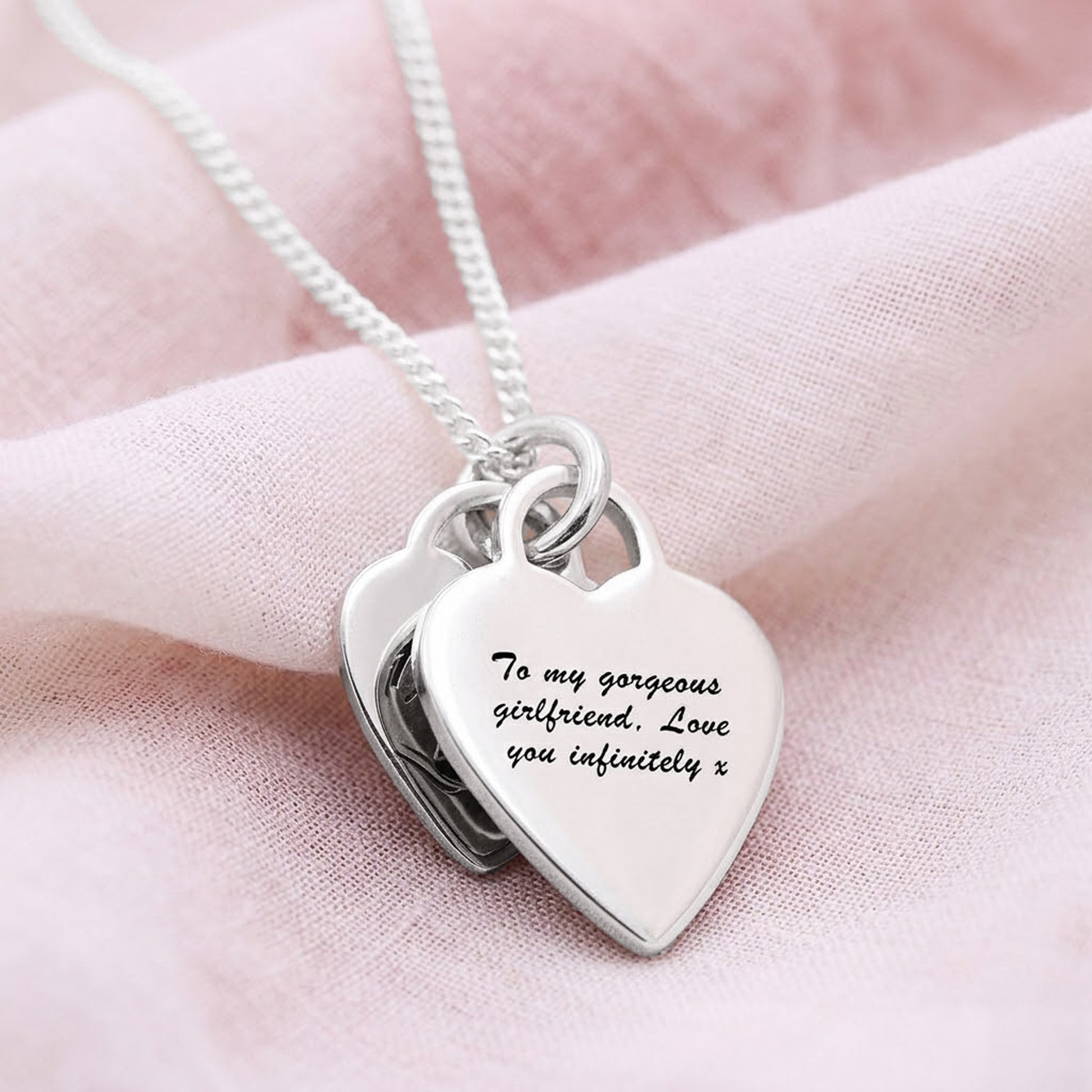 Heart-shaped silver pendant with engraved message on a pink fabric background