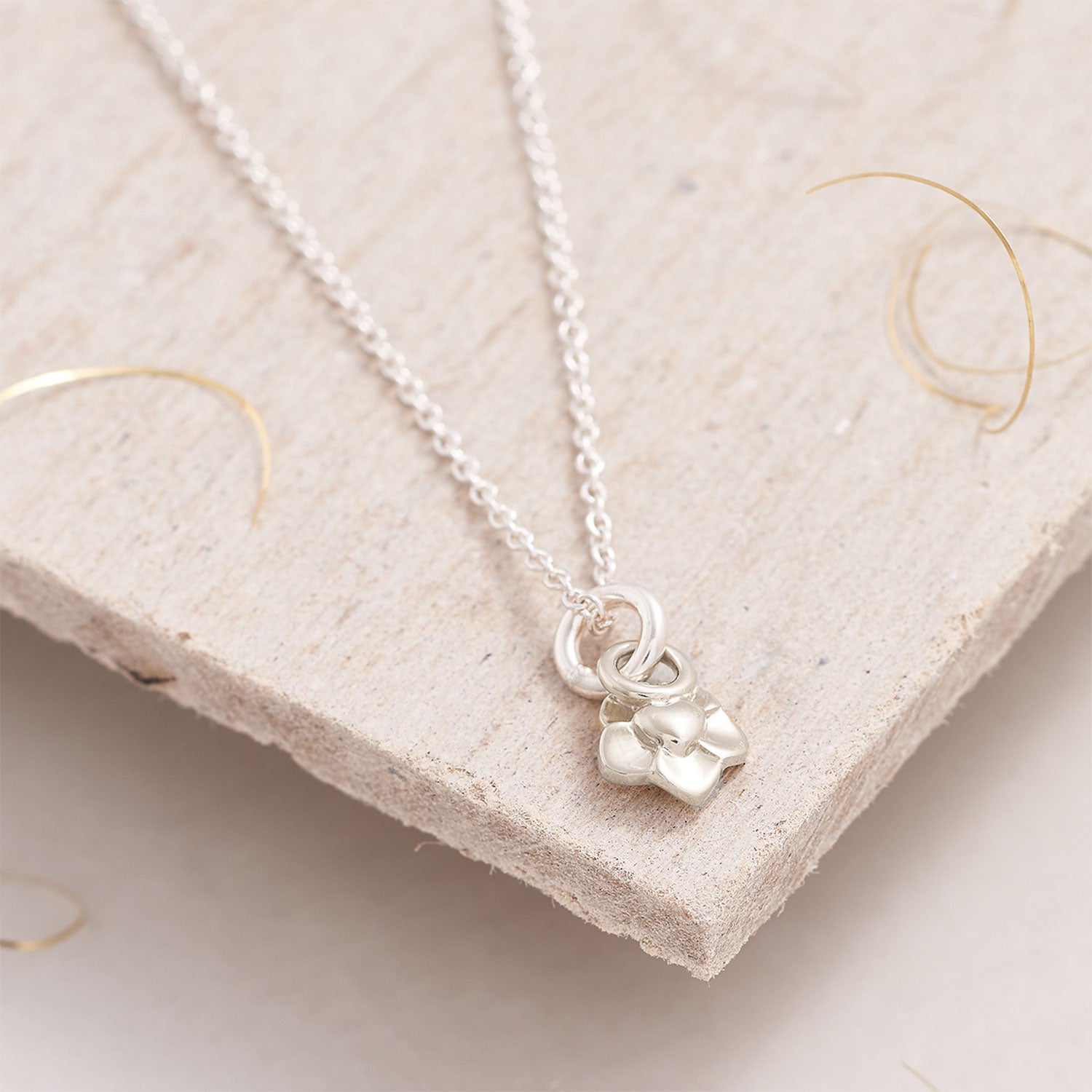 Silver necklace with a small flower pendant on a textured beige surface