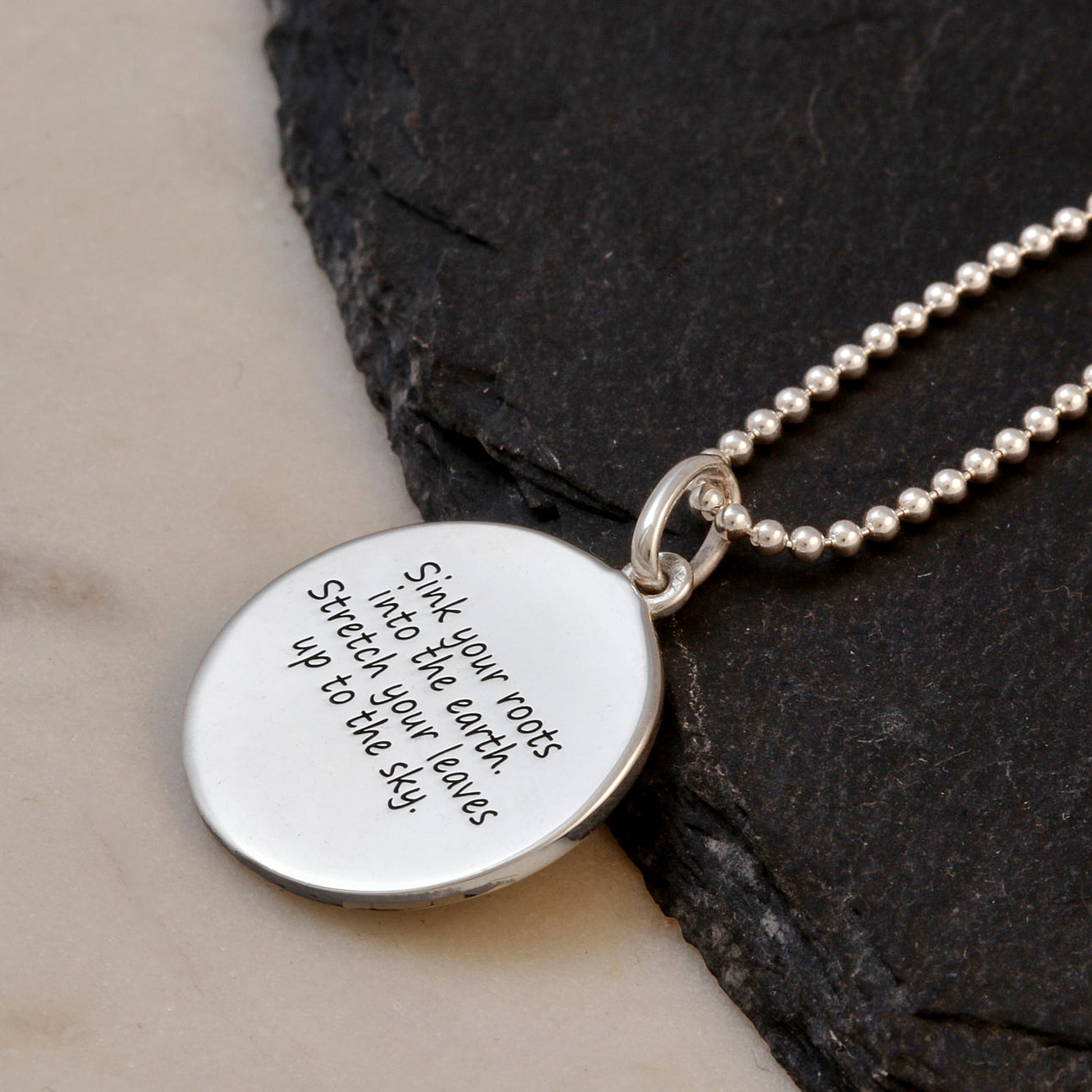 side view of engraved back of tree of life necklace on a dark stone surface