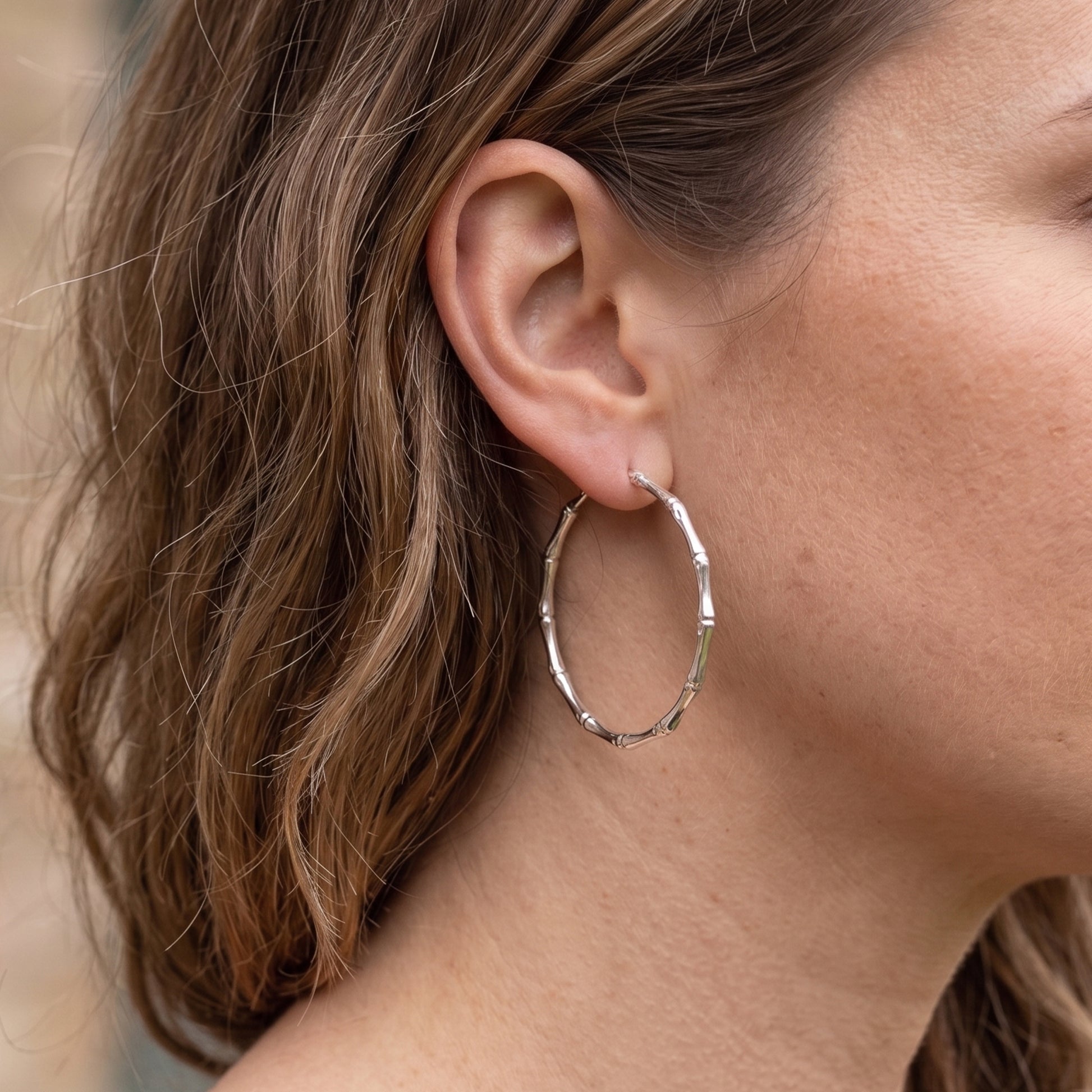 Close-up of a person wearing silver hoop earrings with blurred background